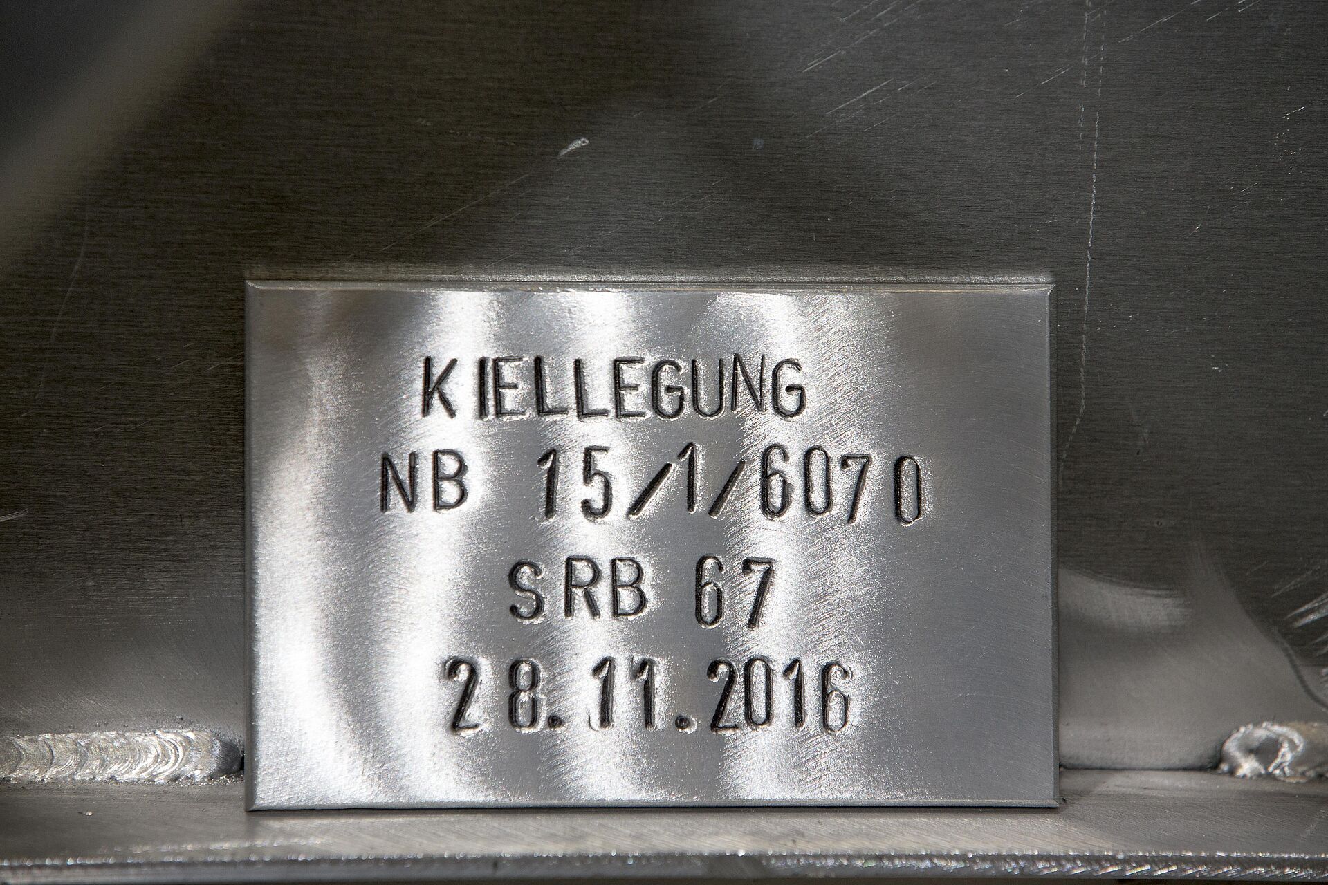 Detailaufnahme eines Akluminiumschildes im Rumpf eines Seenotrettungsbootes. Es zeigt das Datum und mehrere eingestanzte Baunummern.