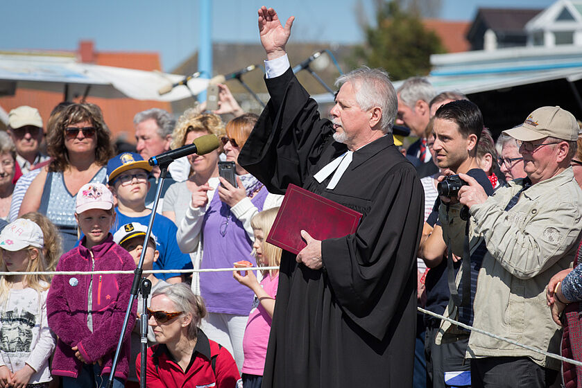 Pastor steht mit erhobener Hand vor Menschenmenge