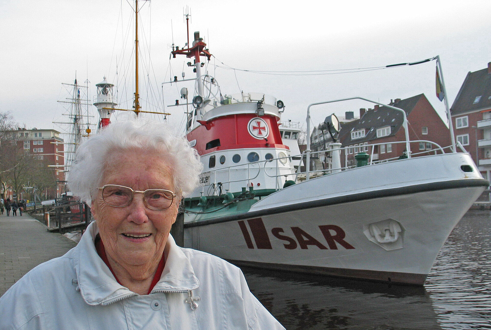 Eine alte Dame steht vor einem Seenotrettungskreuzer im Hafen