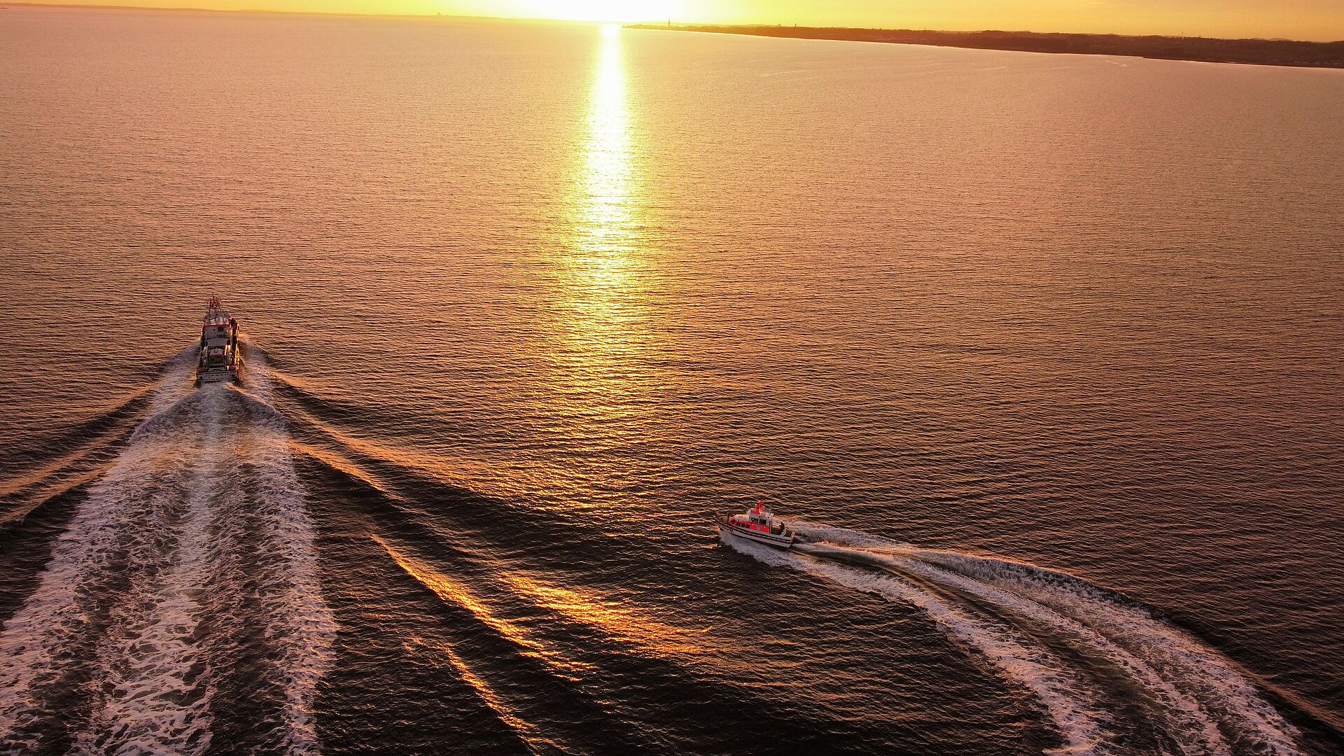 Ein Seenotrettungskreuzer und ein Seenotrettungsboot fahren in den Sonnenuntergang