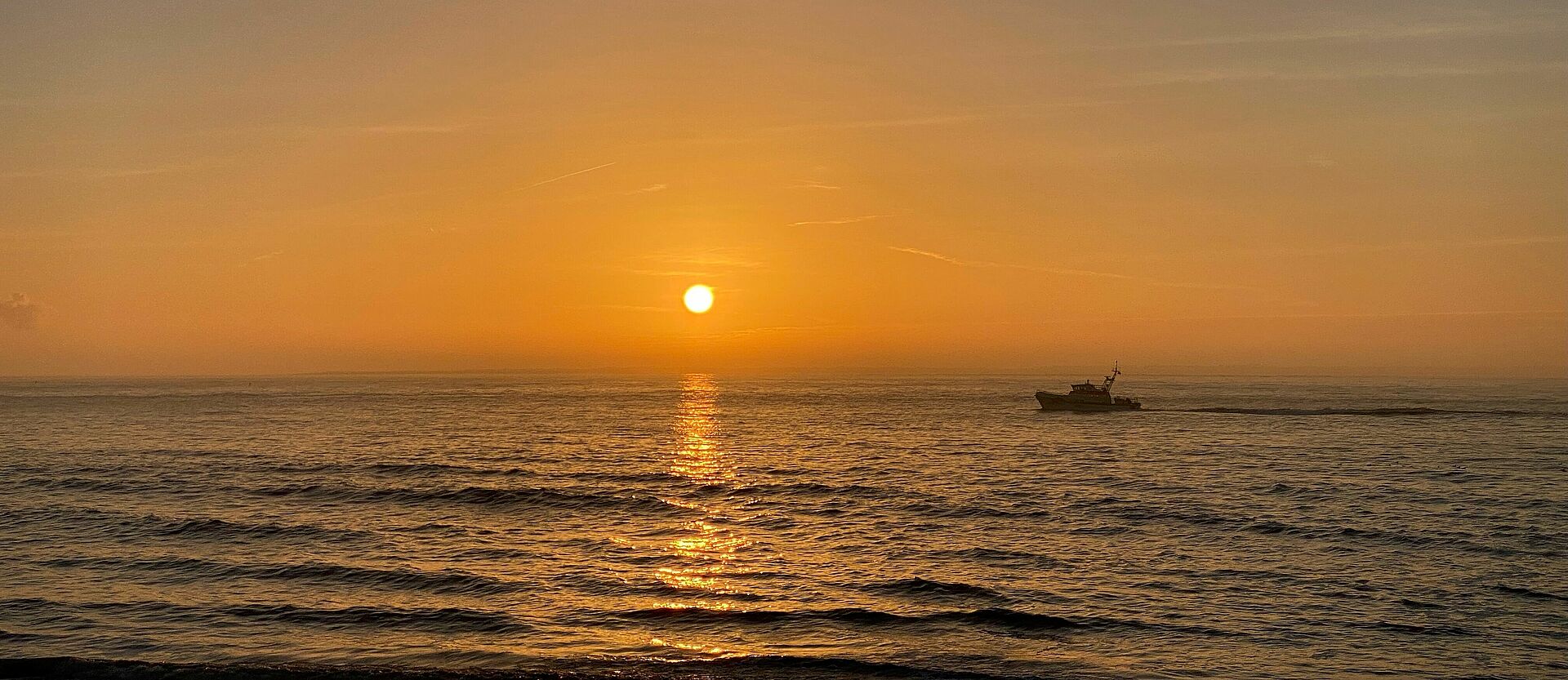 Ein Seenotrettungskreuzer fährt während dem Sonnenuntergang auf den Horizont zu.