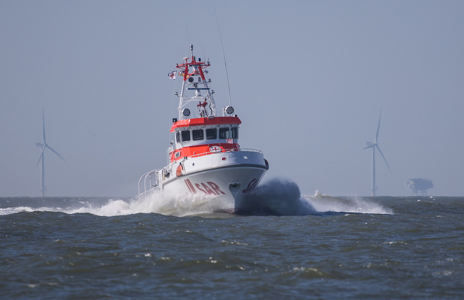 Seenotrettungskreuzer HAMBURG der DGzRS auf der Nordsee, im Hintergrund ist ein Offshore-Windpark zu sehen