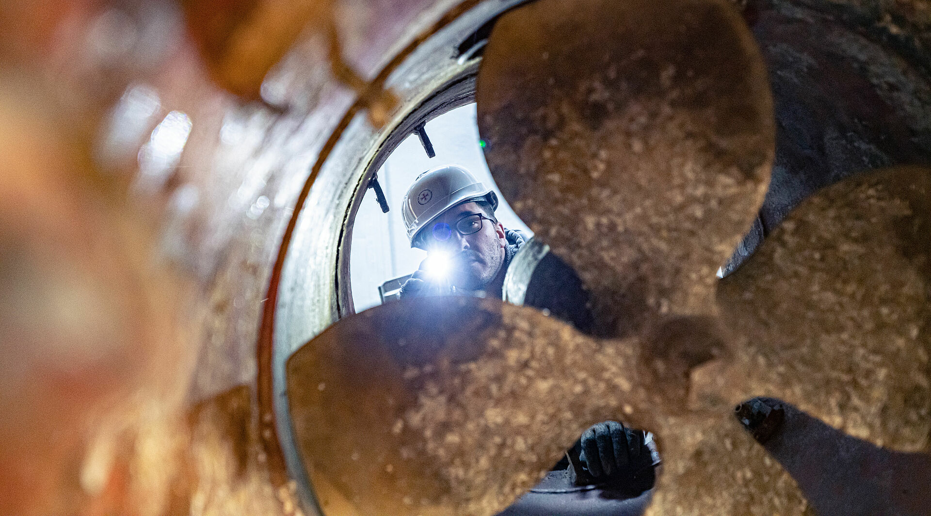 Ein Arbeiter mit Helm leuchtet mit einer Taschenlampe durch die Schraube eines Bugstrahlers im Rumpf eines Seenotrettungskreuzers.