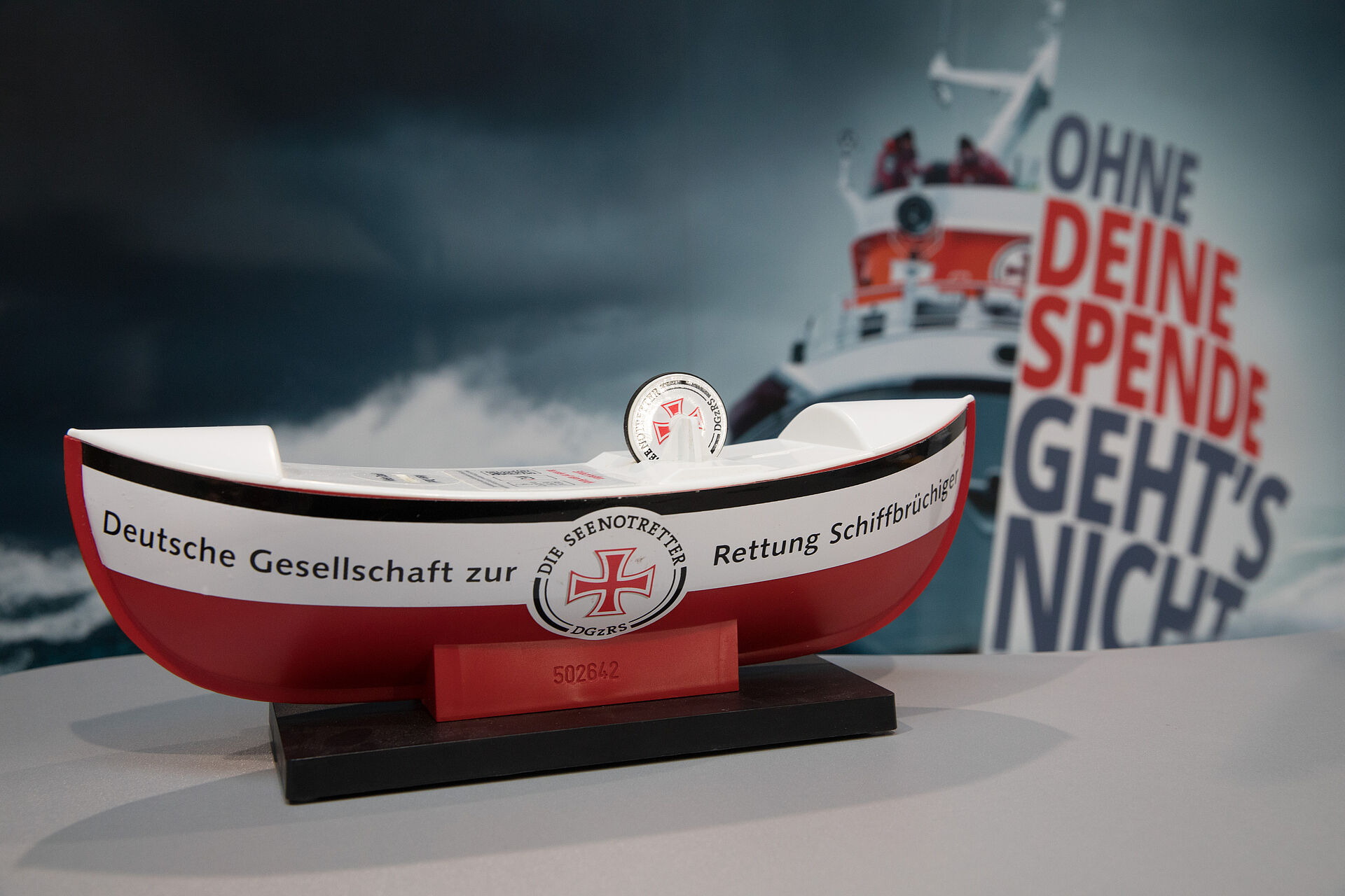 Seenotretter-Sammelschiffchen vor einer Grafik mit der Aufschrift "Ohne deine Spende geht´s nicht"