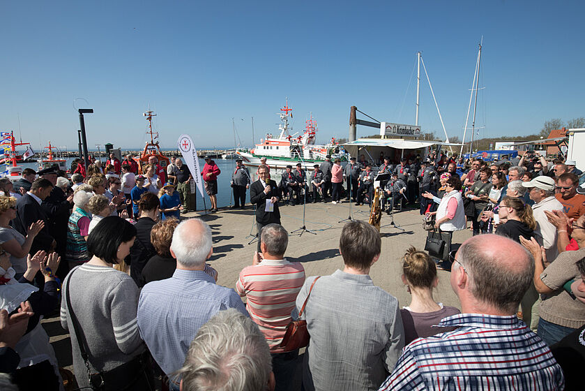 Ein Mann hält eine Rede am Hafenbecken, umringt von vielen Menschen