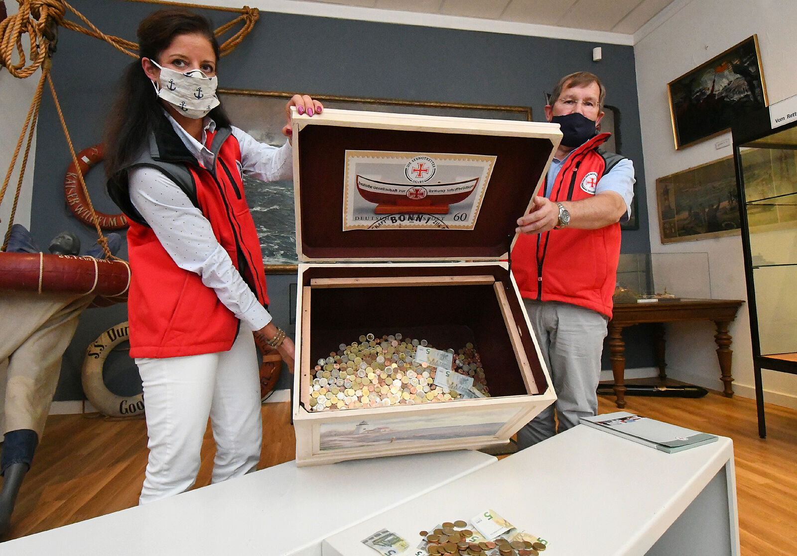 Zwei Seenotretter halten eine Kiste mit den Spenden der Museumsbesucher in den Händen