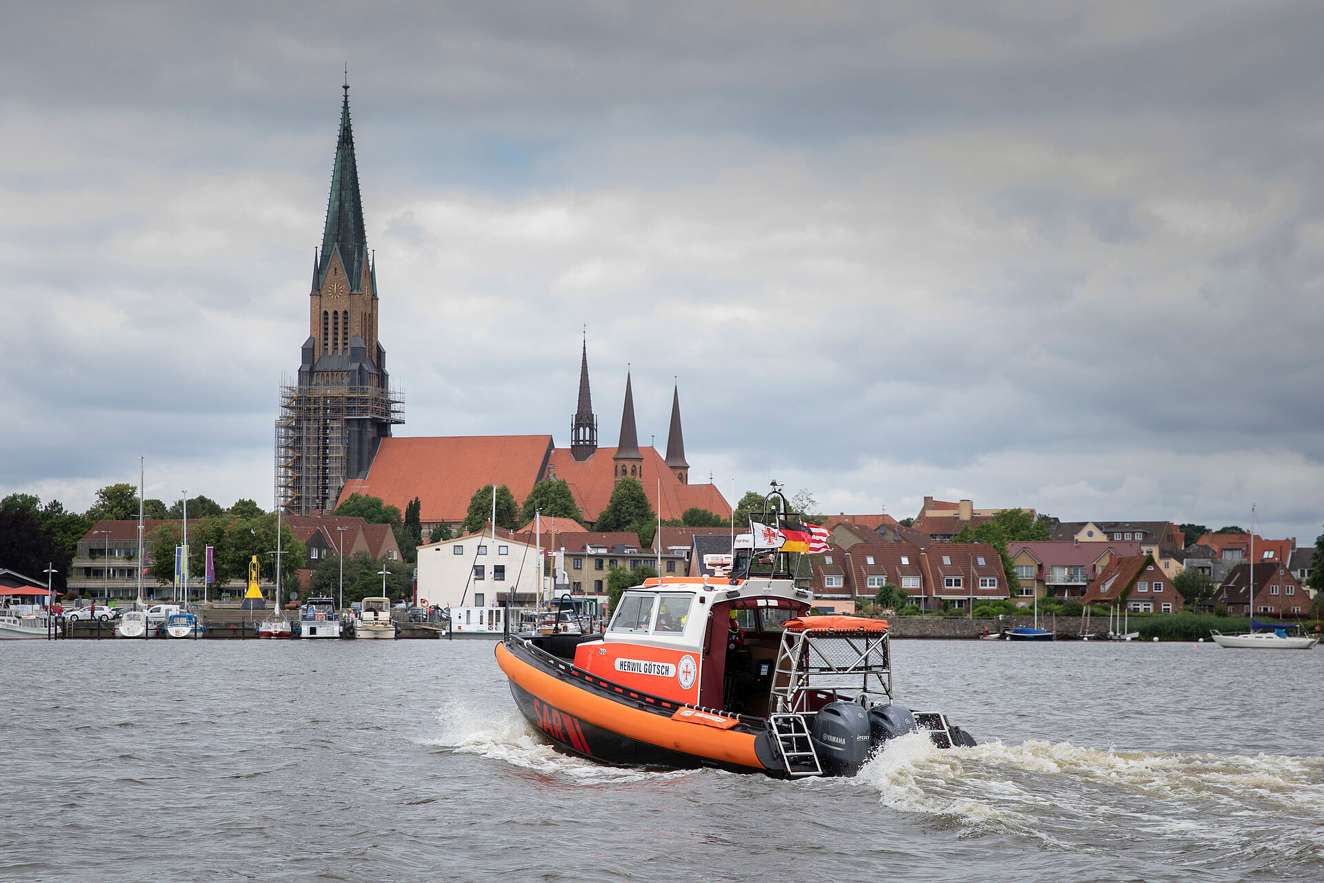 Das Seenotrettungsboot HERWIL GÖTSCH fährt in langsamer Fahrt von der Schlei Richtung dem Schleswiger Stadthafen. Die markante Kulisse mit der Schleswiger Kirche im Hintergrund.