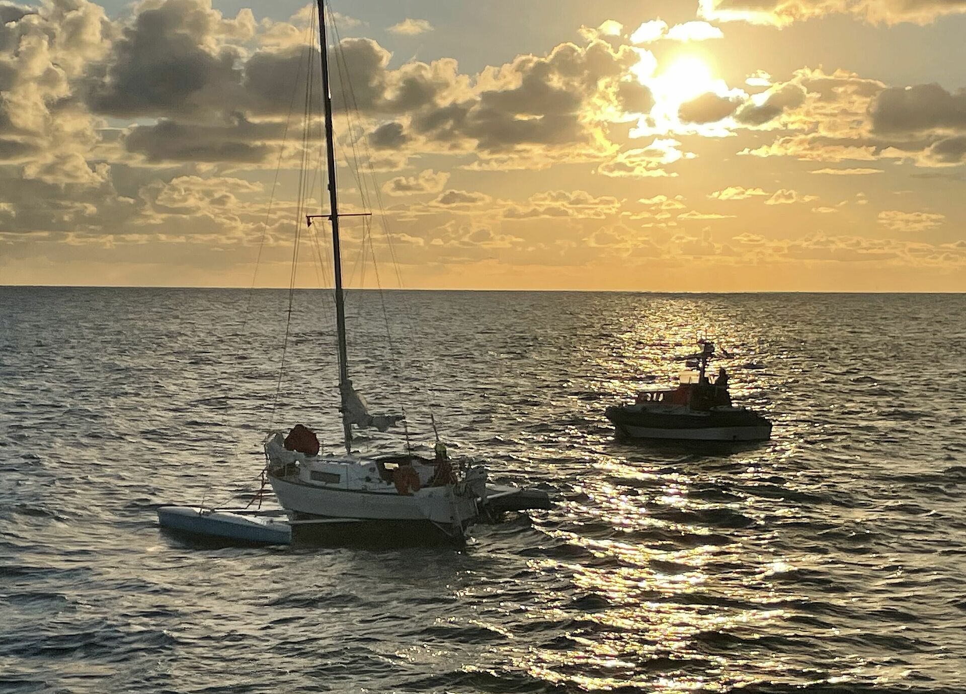 Das Tochterboot eines Seenotrettungskreuzer kommt im Sonnenaufgang auf der Nordsee einem Trimaran zu Hilfe.