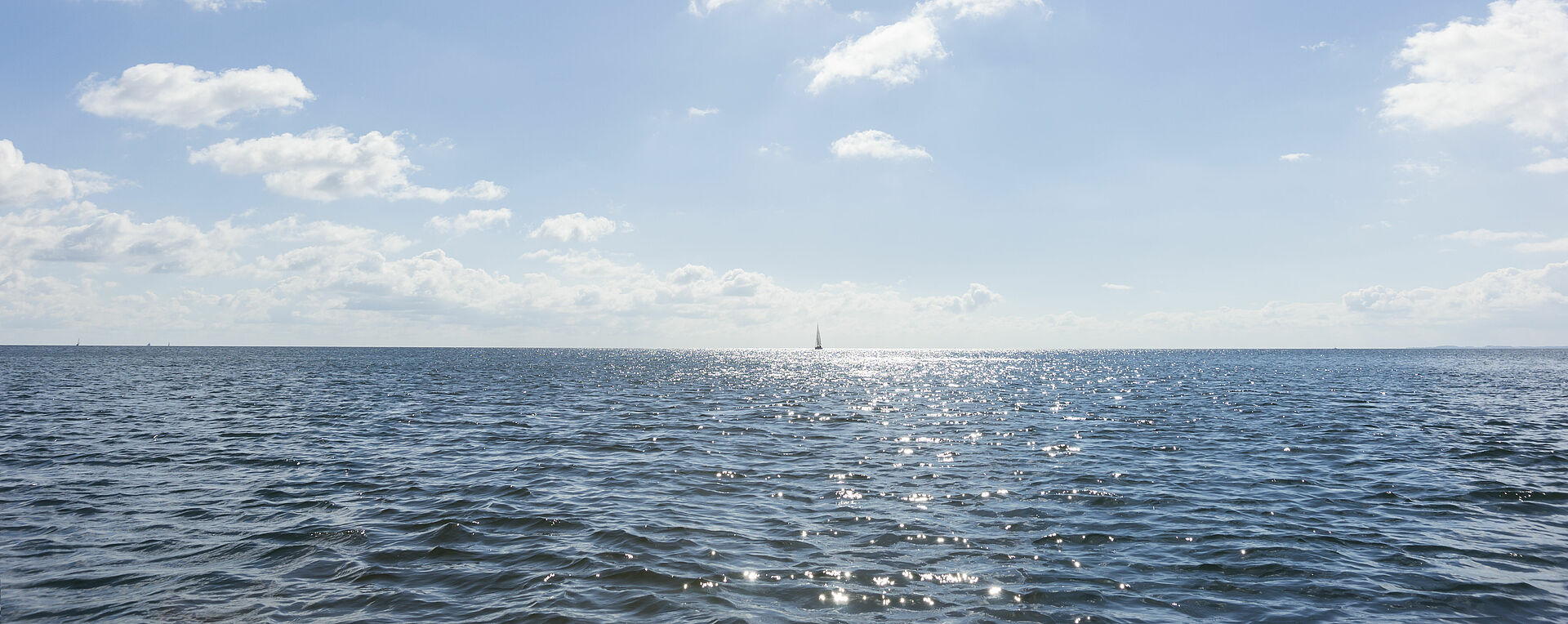 Die Sonne spiegelt sich im klaren Wasser der Ostsee am Horizont.