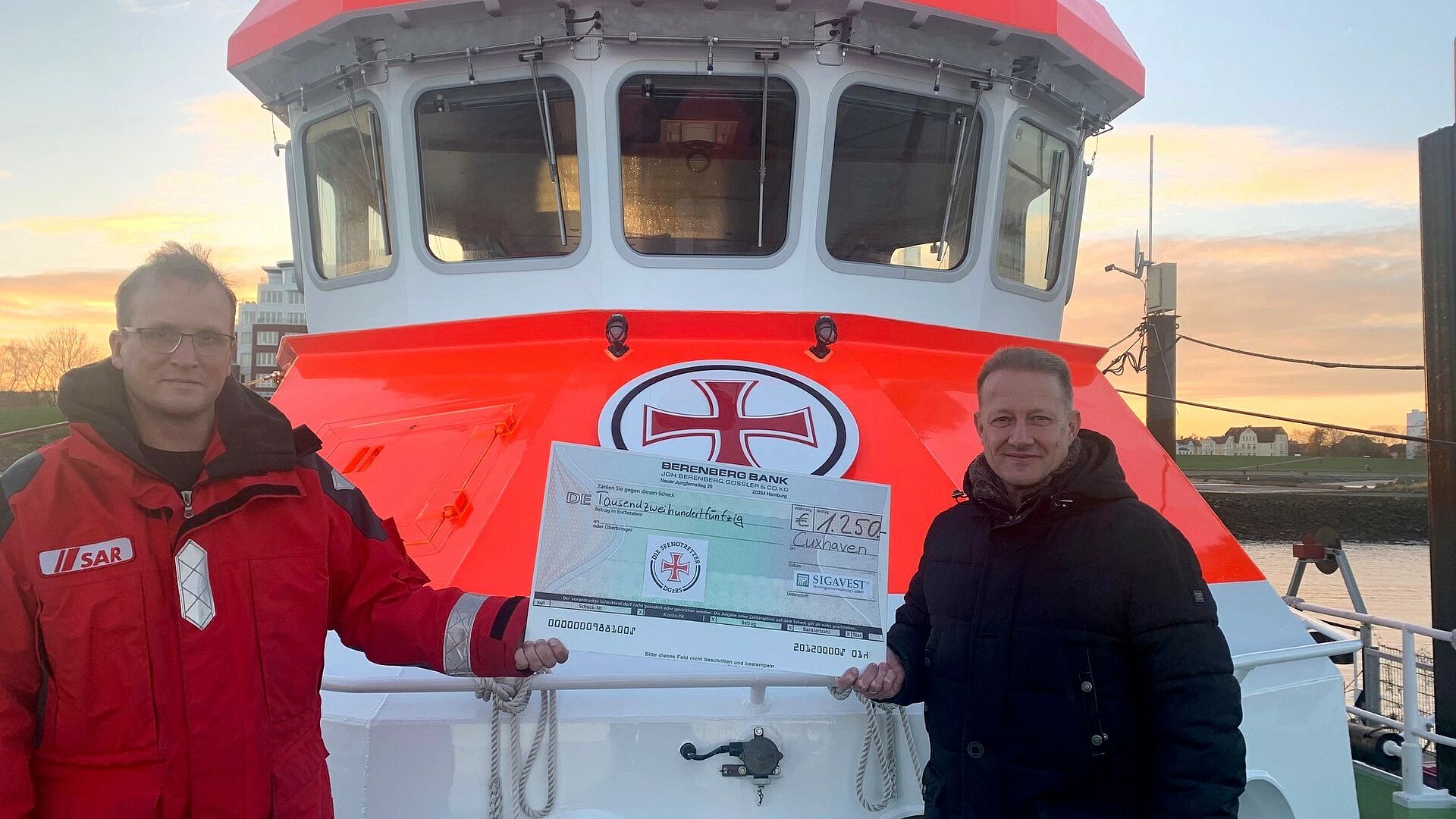 An Bord des Seenotrettungskreuzers ANNELIESE KRAMER/Station Cuxhaven nimmt Vormann Hanno Renner (l.) einen symbolischen Spendenscheck von Sigavest-Geschäftsführer Christian Mallek entgegen.