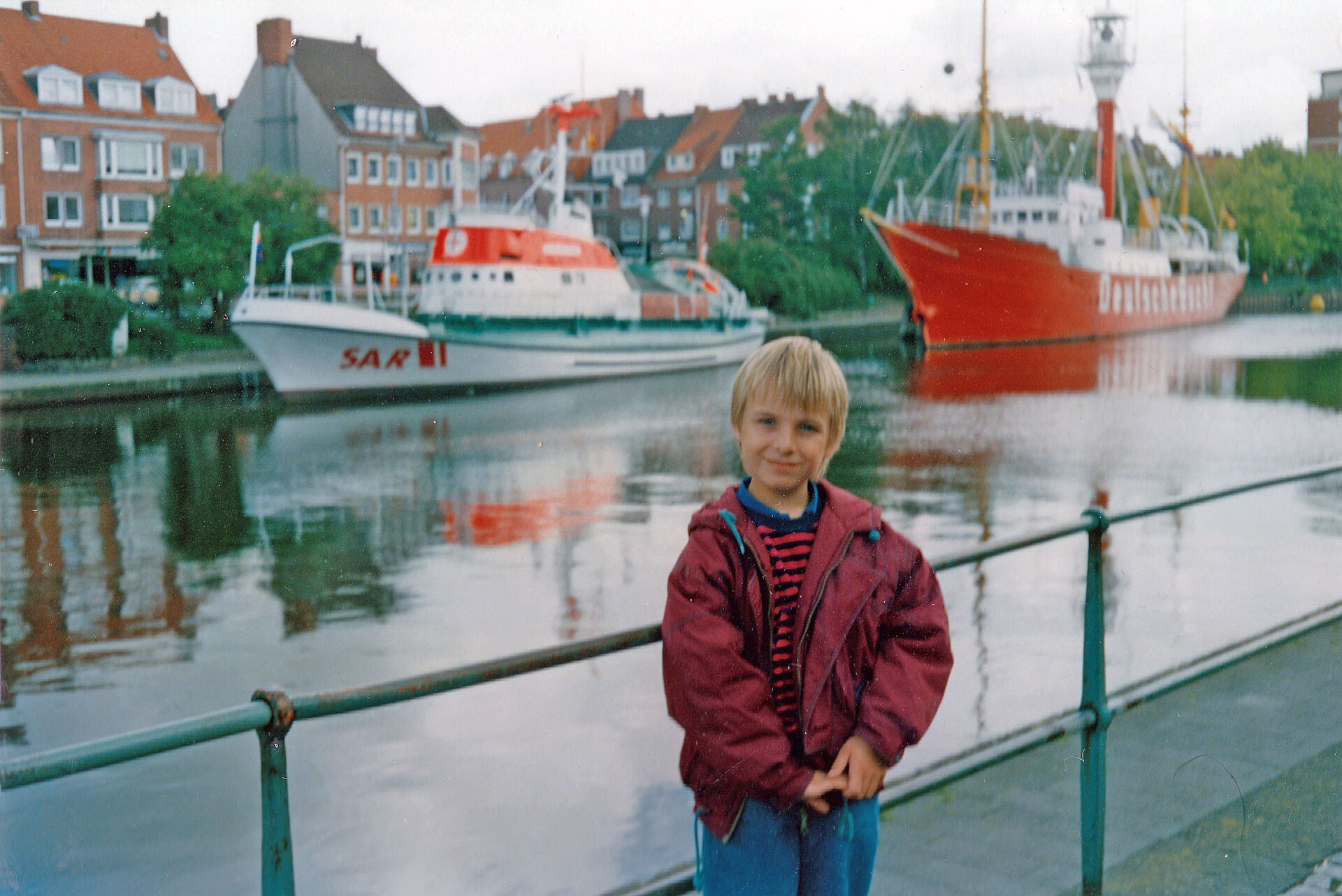 Ein Kind vor einem Kanal, im Hintergrund sind zwei Schiffe zu sehen.