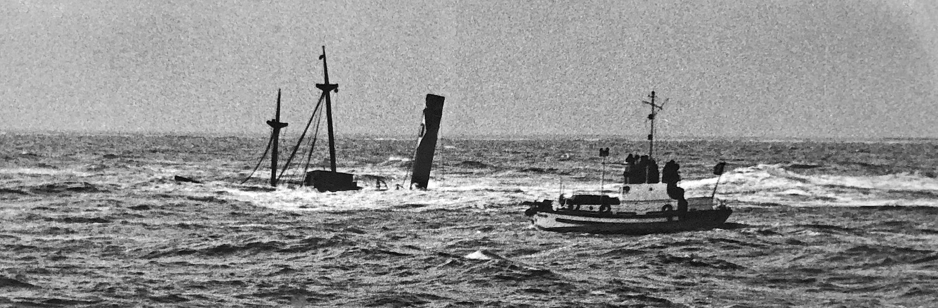 Schwarz-Weiß-Foto eines Motorrettungsbootes der Seenotretter an einem untergegangenen Dampfschiff