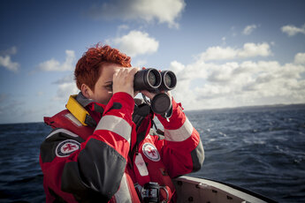 Seenotretterin in Uniform schaut durch Fernglas auf hoher See