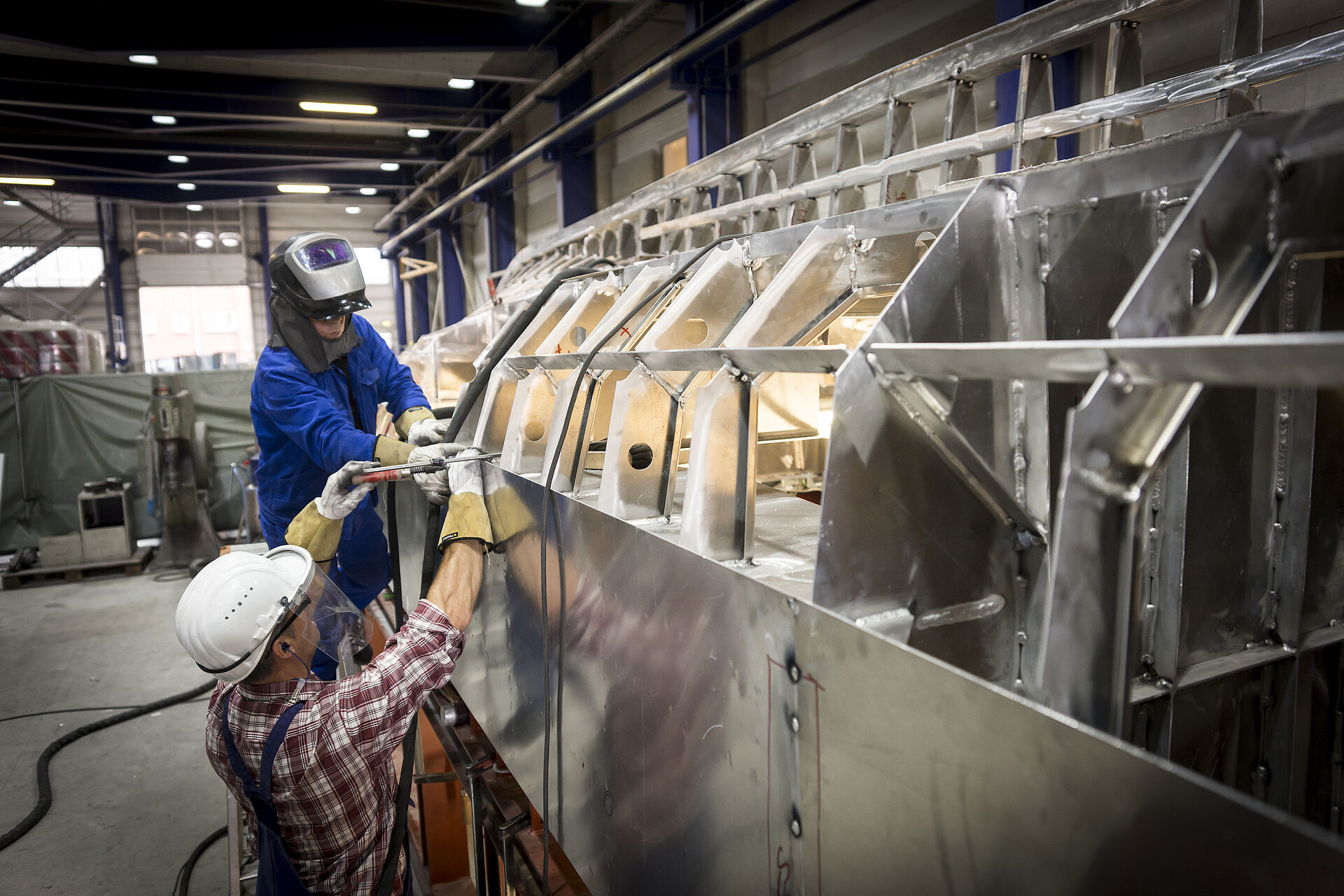 Zwei Werftmitarbeiter arbeiten am Aluminium-Netzspantengerüst eines Seenotrettungsboot in der Werfthalle.
