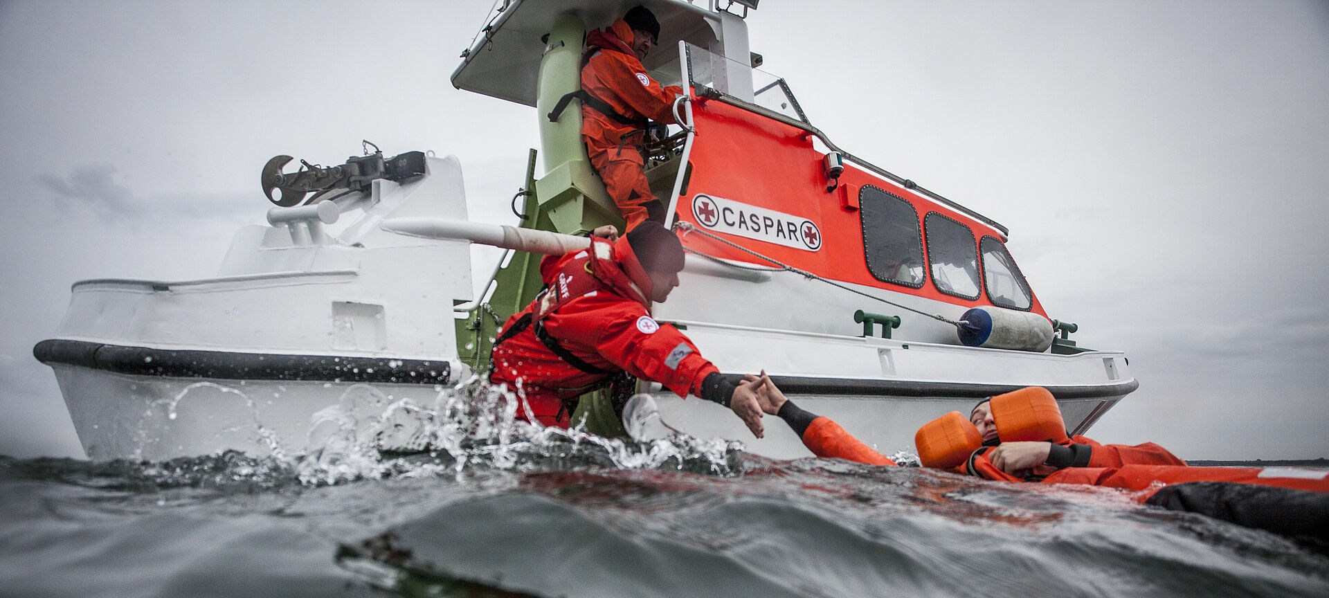 Ein Seenotretter holt einen Menschen aus dem Wasser auf ein Tochterboot eines Seenotrettungskreuzers.