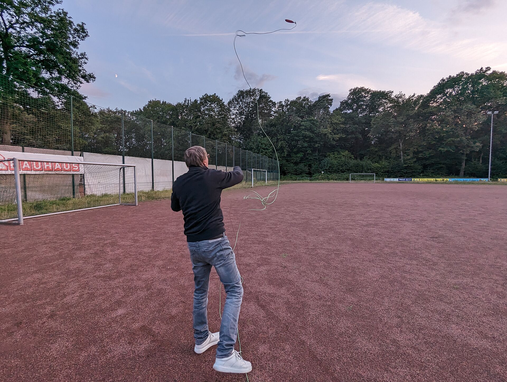 Auf einem Sportfeld wirft ein Mann, von hinten zu sehen, eine Leine mit einem Gewicht daran durch die Luft, da er übt, auf dem Trockenen eine Leinenverbindung herzustellen.