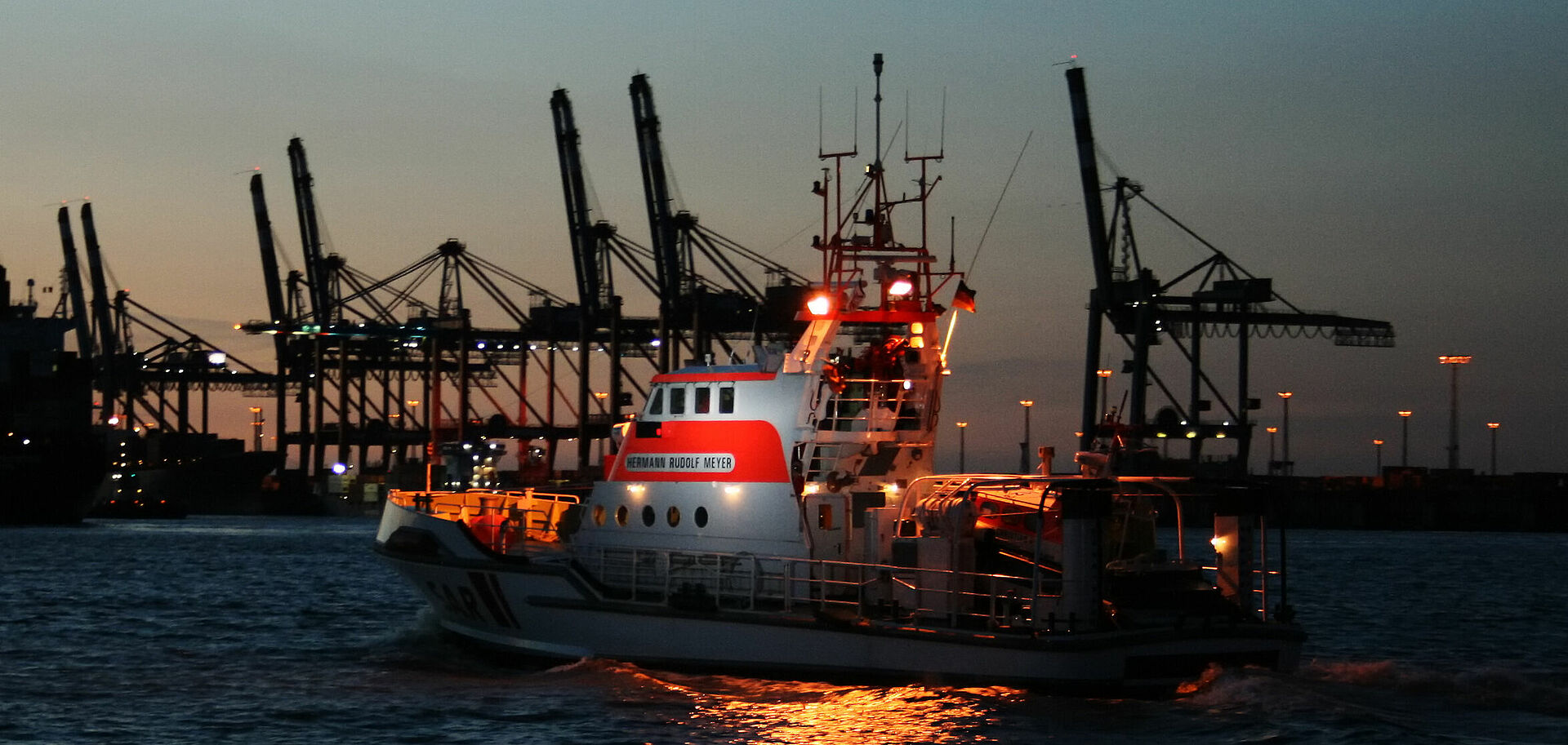 Seenotrettungskreuzer HERMANN RUDOLF MEYER vor Hafenkulisse im Sonnenuntergang