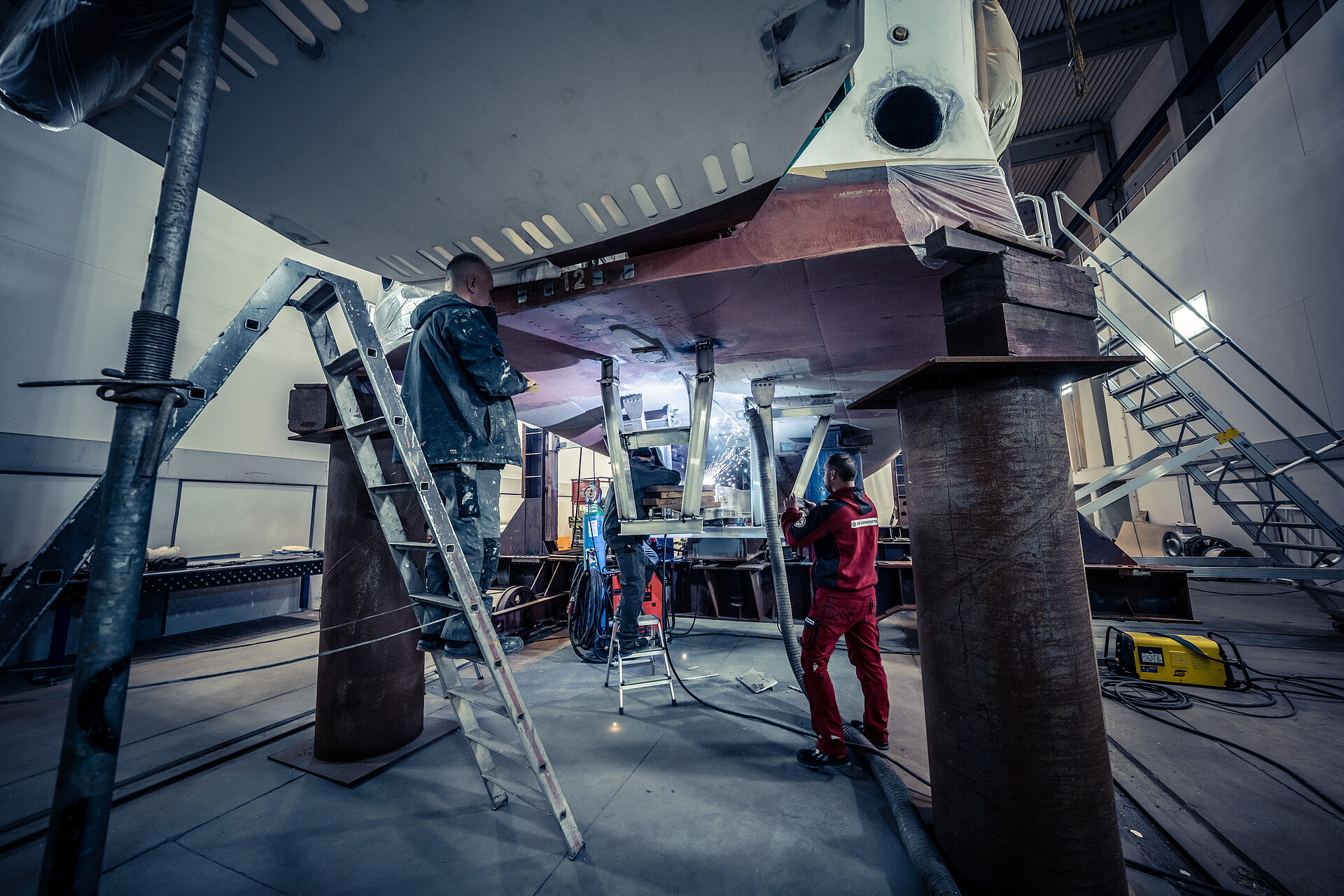 Arbeiten unter dem Kiel des Seenotrettungskreuzers EUGEN bei geöffneter Heckklappe: Ein Werftarbeiter schweißt, es fliegen Funken.