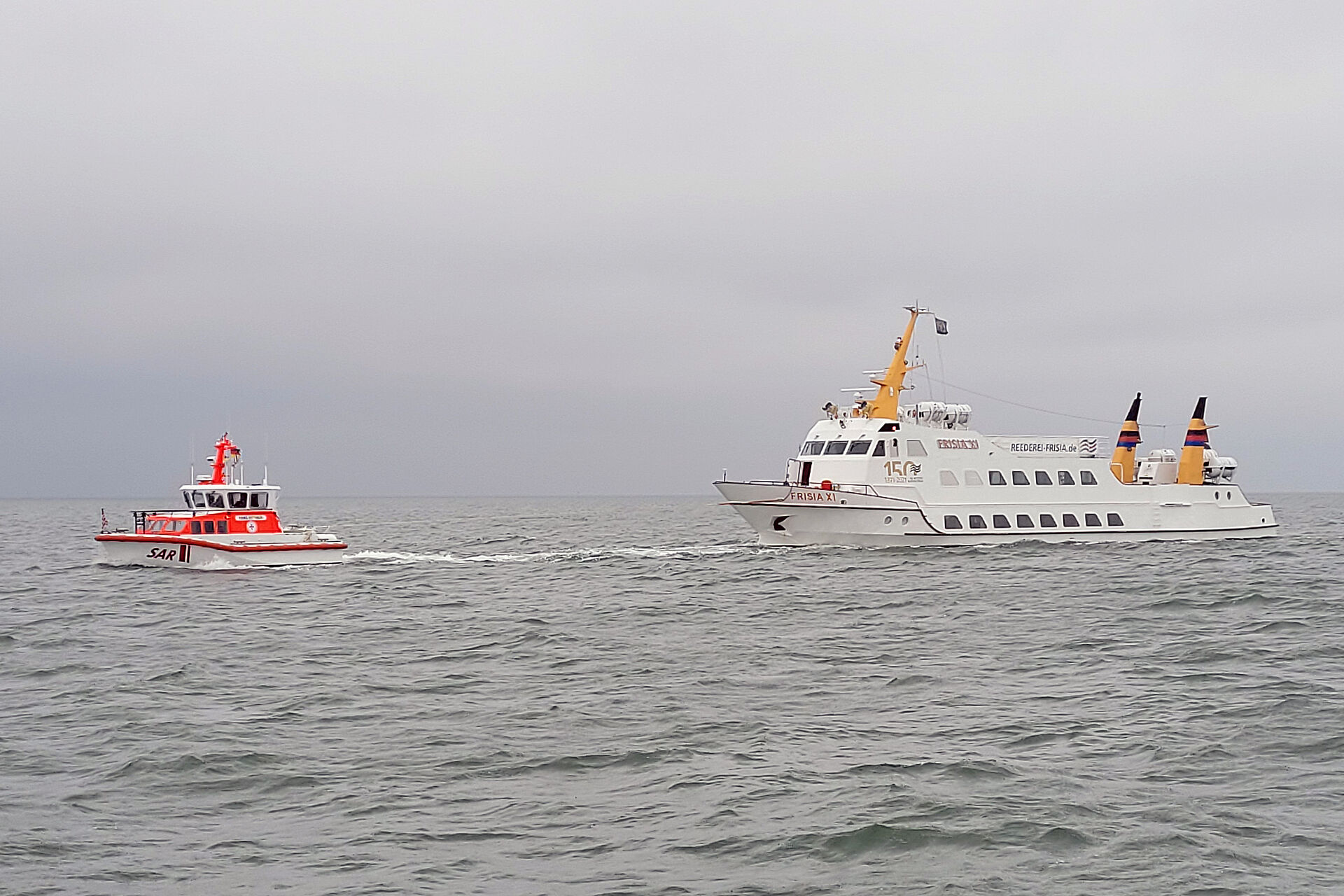 Seenotrettungskreuzer fährt vor der Inselfähre vor Juist