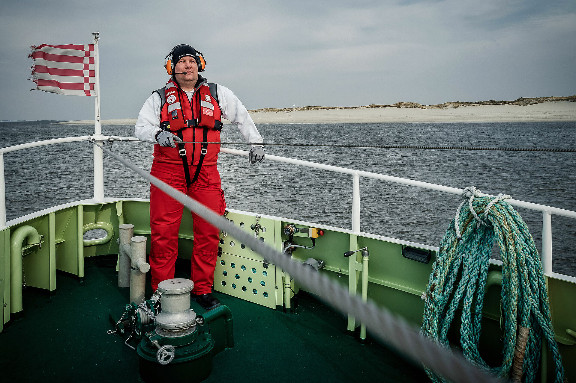 Ein Seenotretter mit Gehörschutz steht an Deck eines Seenotrettungskreuzers