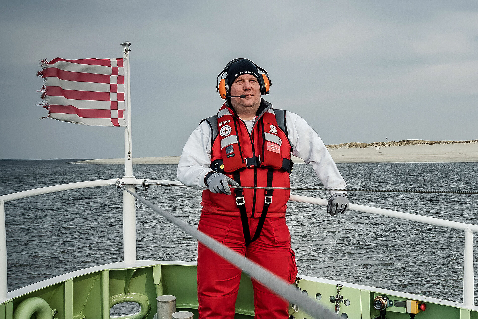 Ein Seenotretter mit Gehörschutz steht an Deck eines Seenotrettungskreuzers