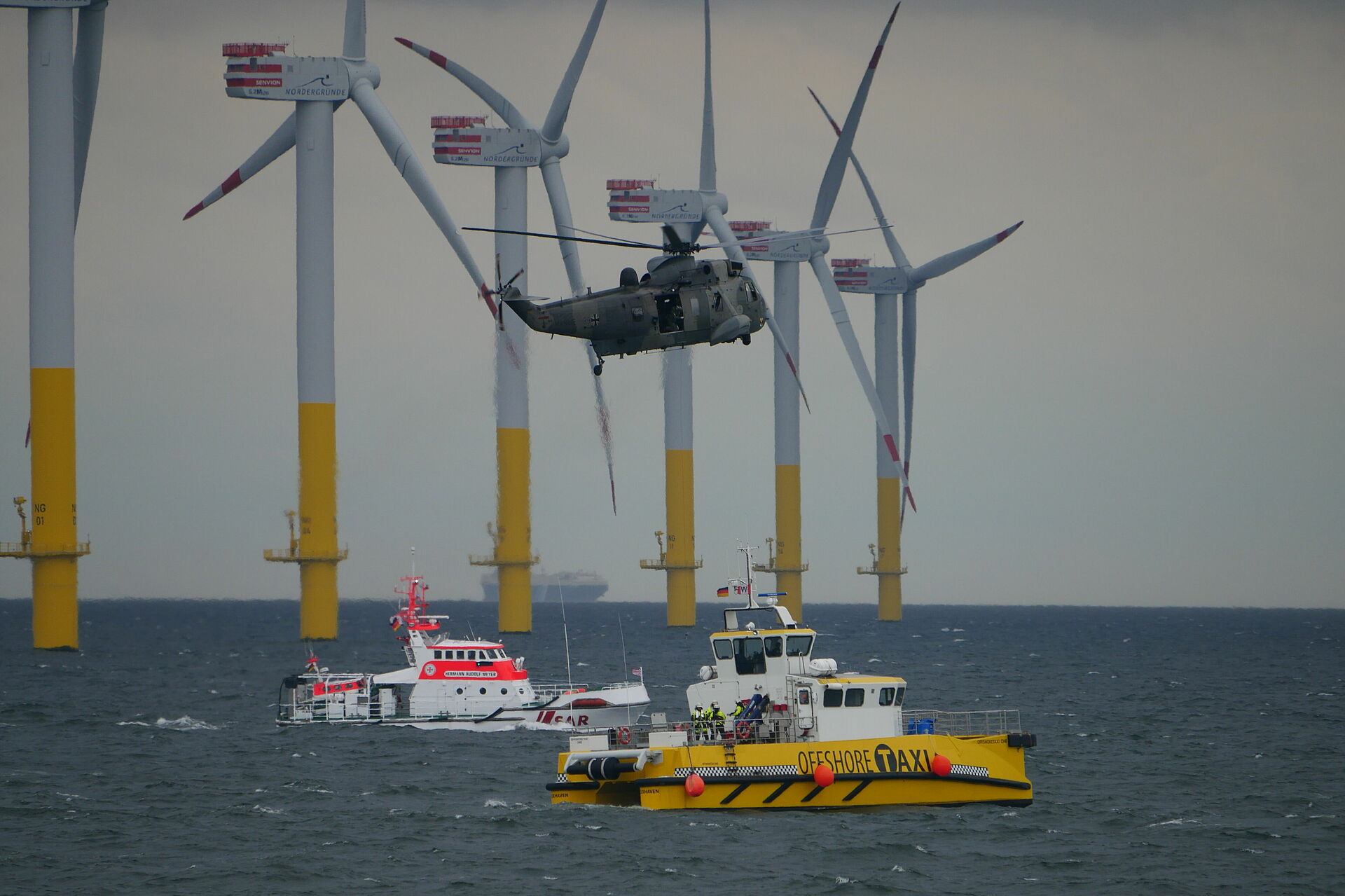 Hubschrauber und Seenotrettungskreuzer im Einsatz für ein Schiff in der Nähe eines Windparks