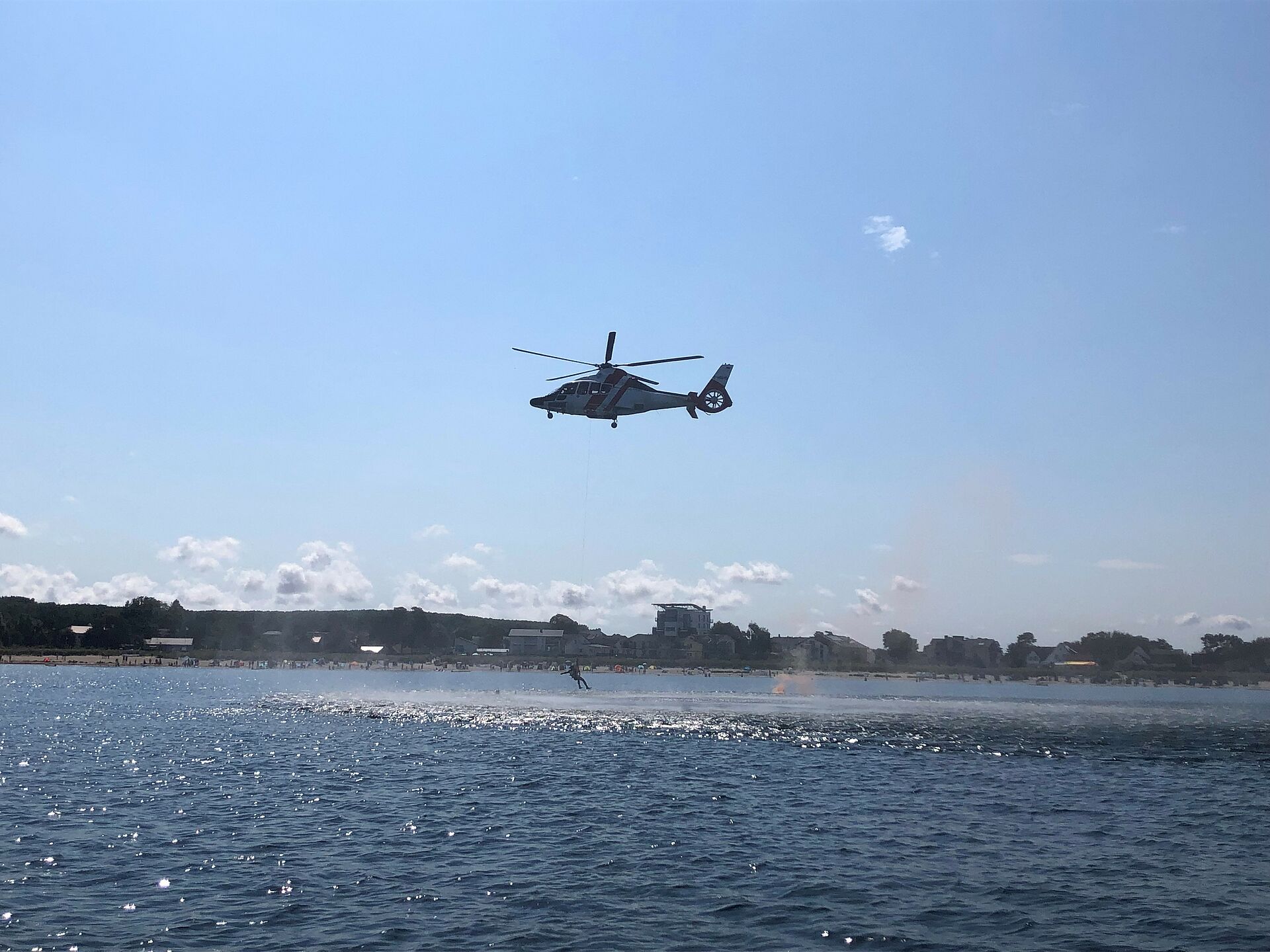 Hubschrauber steht über dem Wasser und an einem Seil hängt ein Mensch