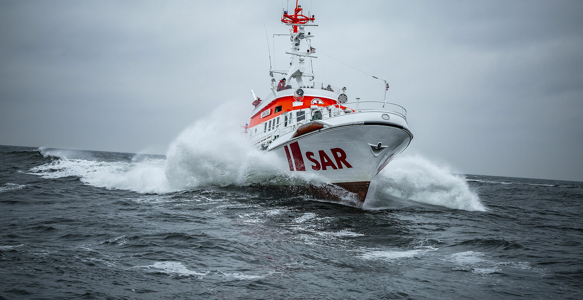 Seenotrettungskreuzer ARKONA fährt in schneller Fahrt durch die Ostsee. Wellen schlagen Gischt seitlich am Schiff.