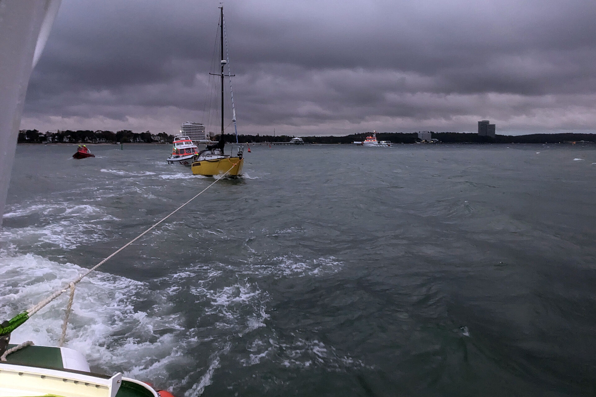 Ein Seenotrettungsboot hat ein Segelboot in Schlepp genommen. Das rot-weiße Tochterboot eines Seenotrettungskreuzers im Hintergrund sichert den Schleppanhang ab. Dunkle Wolken haben sich über der Ostsee gebildet.