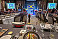 Blick auf eine Essenstafel mit Gästen in blau-weiß-gestreiften Fischerhemden an den Tischen sitzend. Im Vordergrund ein eingedeckter Tisch, auf dem neben dem Geschirr das Seenotretter-Sammelschiffchen steht.