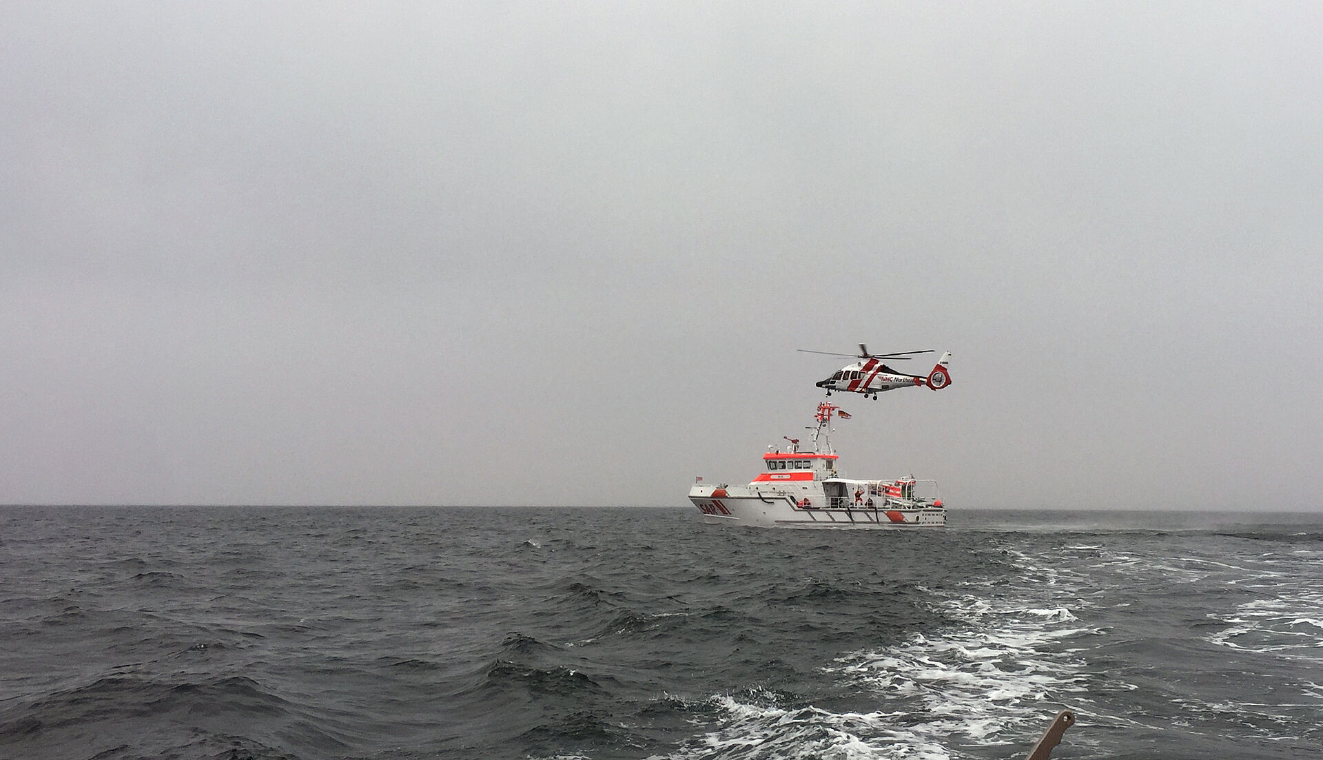 Helikopter fliegt über Seenotrettungskreuzer auf offener See