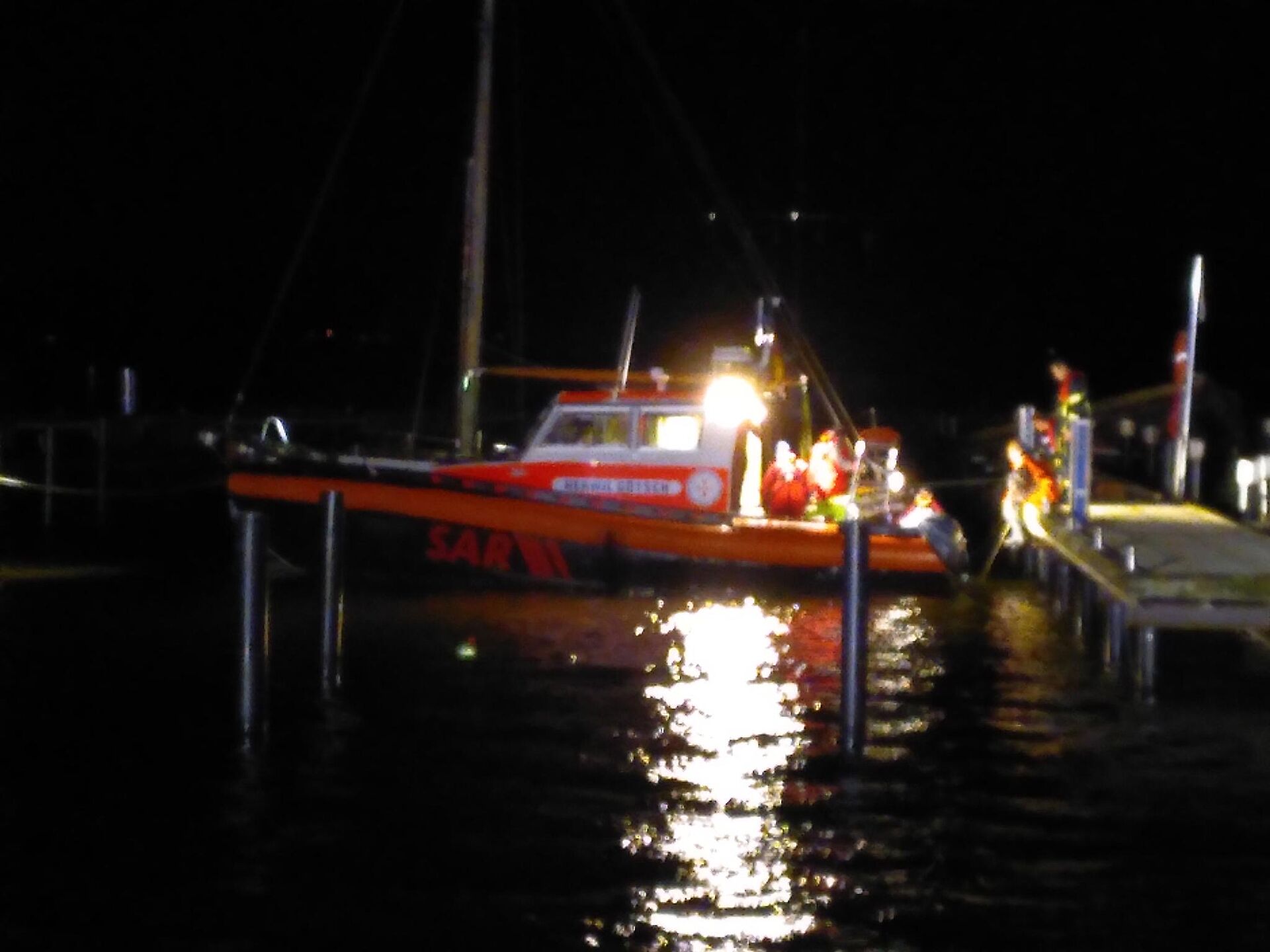 Ein hell erleuchtetes Seenotrettungsboot bei völliger Dunkelheit im Einsatz an einem Steg in einem Hafen