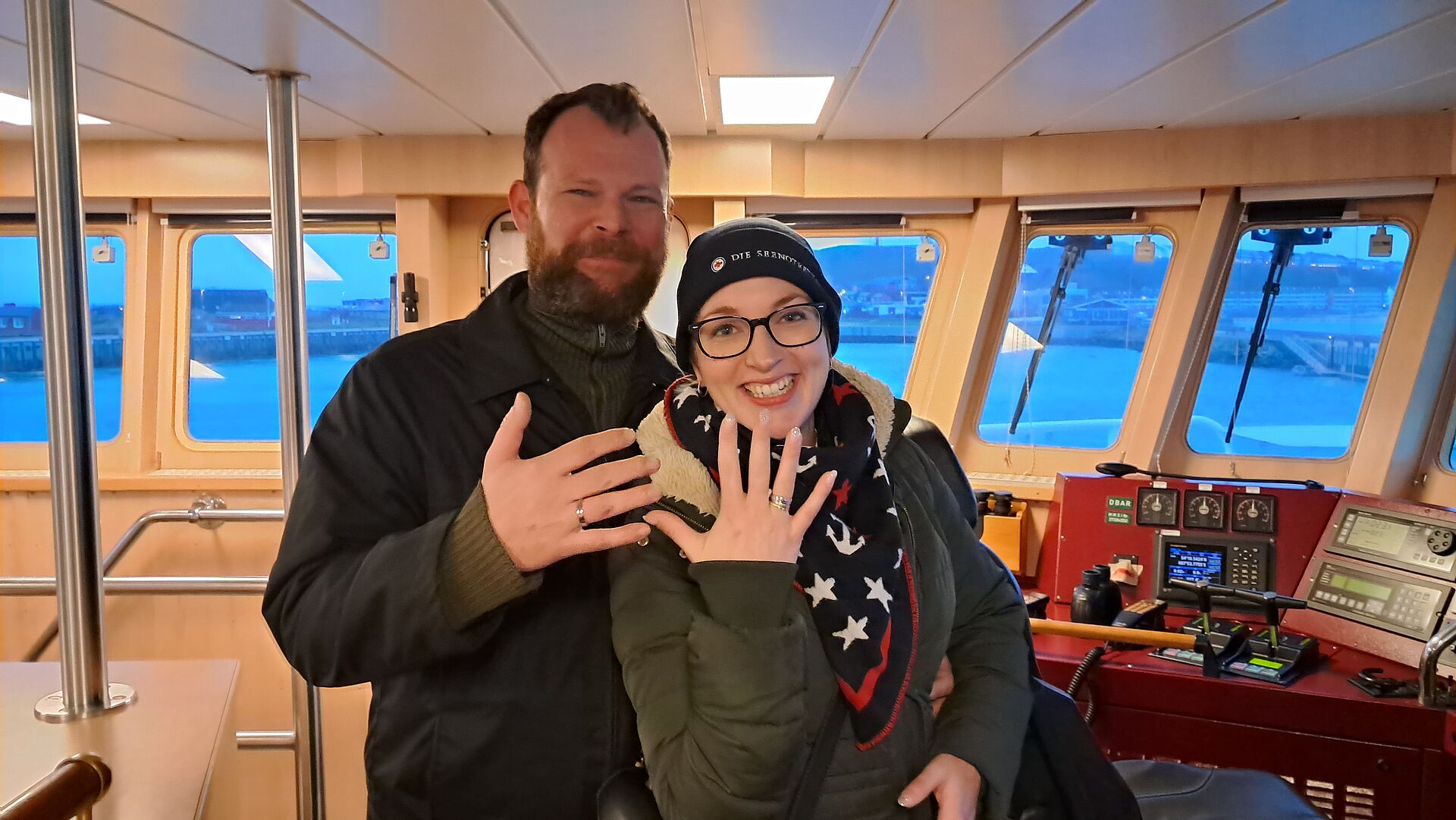 Eine Frau und ein Mann stehen auf der Brücke eines Seenotrettungskreuzers und zeigen ihre Verlobungsringe