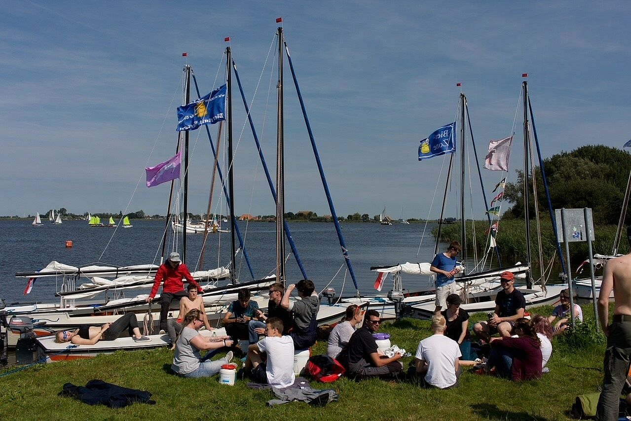 Jugendliche der evangelischen Kirchengemeinde sitzen und liegen vor ihren Segelbooten auf dem Rasen in der Sonne.