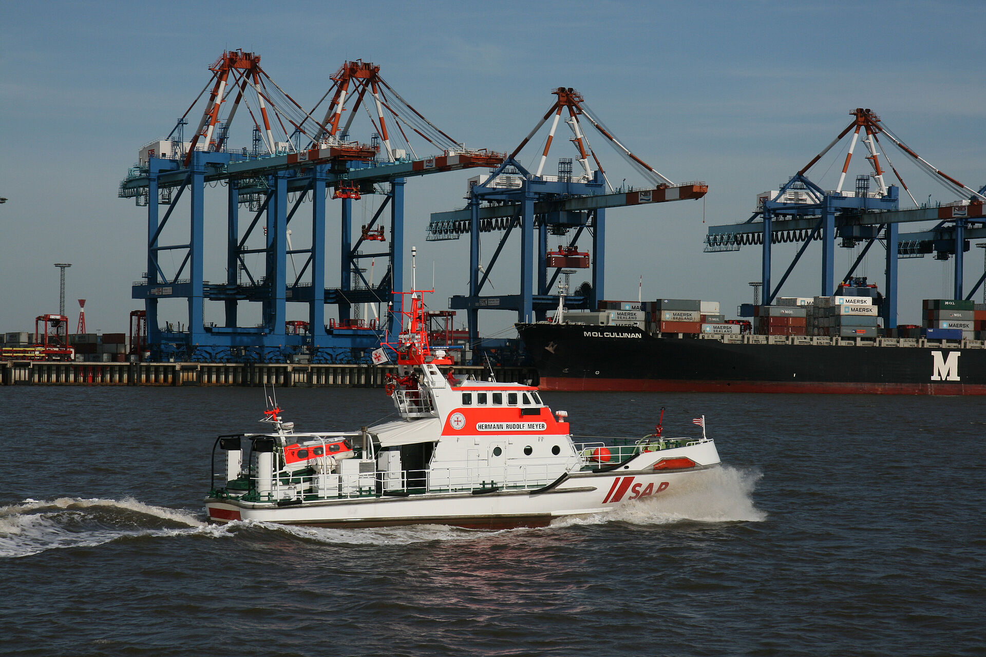 Ein Seenotrettungskreuzer vor den Containerbrücken eines großen Hafens