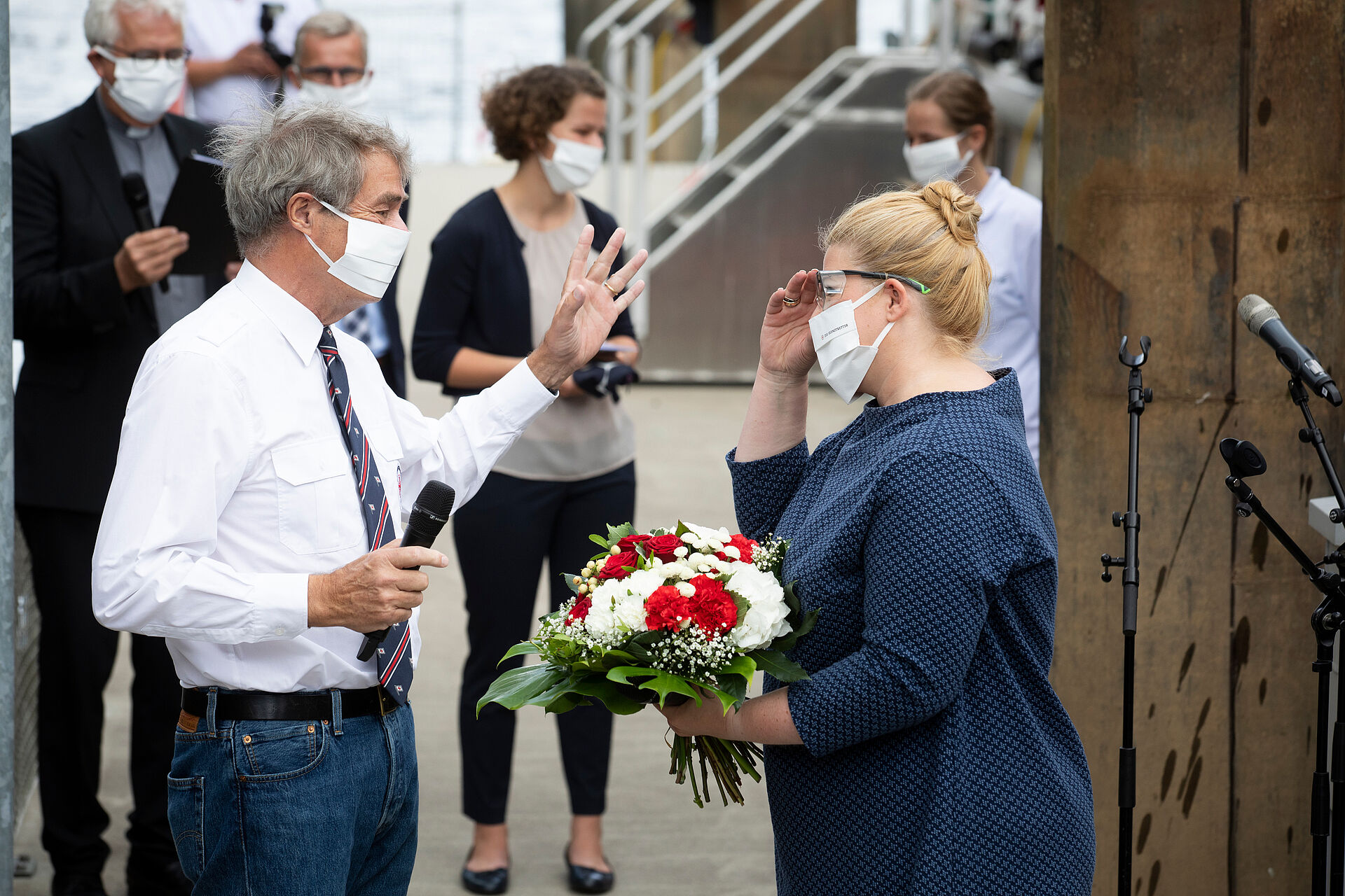 Mann steht mit Mikrofon neben Frau mit Blumenstrauß in der Hand