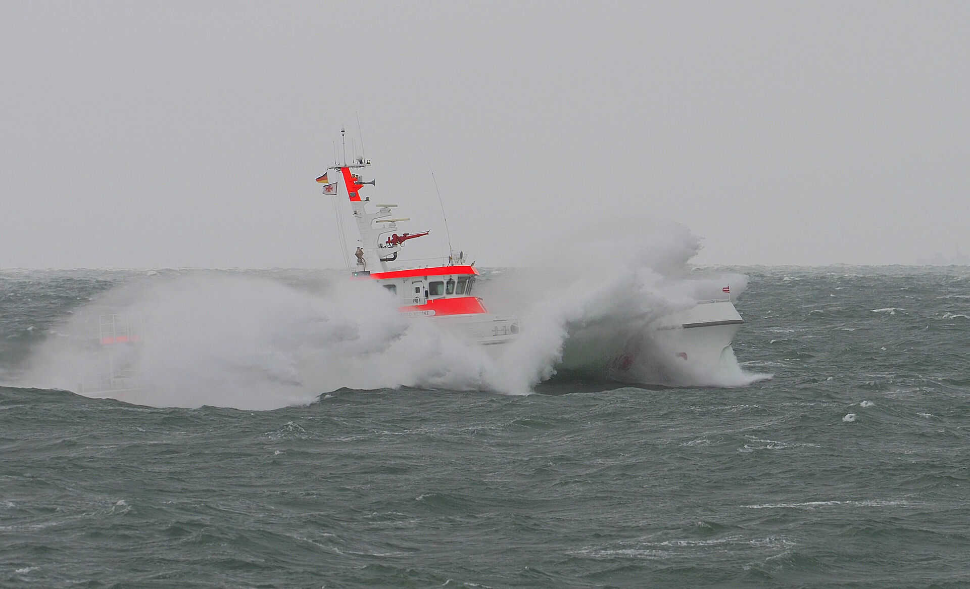 Der Seenotrettungskreuzer HARRO KOEBKE fährt bei nebeligem Wetter durch die Ostsee. Wellen schlagen Gischt gegen das Schiff.