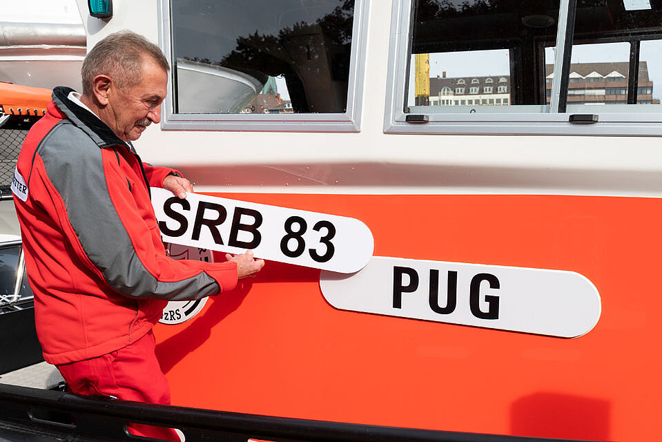 Seenotretter entfernt das Schild mit der Aufschrift SRB83 und enthüllt das Schild mit der Aufschrift PUG