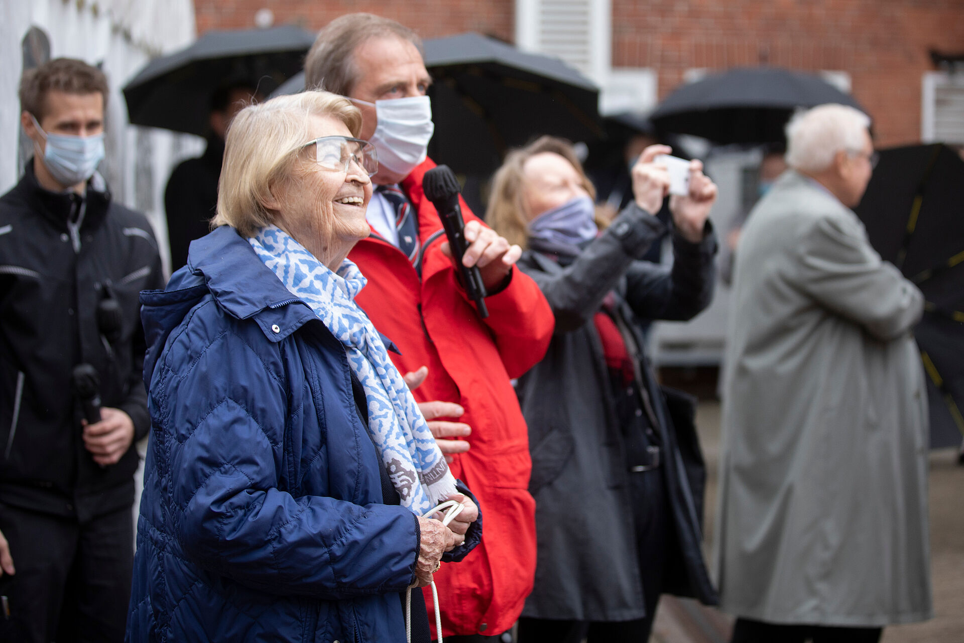 Die Taufpatin in blauer Jacke blick lächelnd nach oben. Hinter ihr steht DGzRS-Vorsitzer Gerhard Harder in roter Regenjacke.