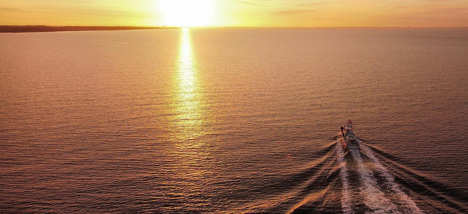 Sonnenuntergang über der Ostsee - ein Seenotrettungskreuzer fährt auf den Horizont zu.