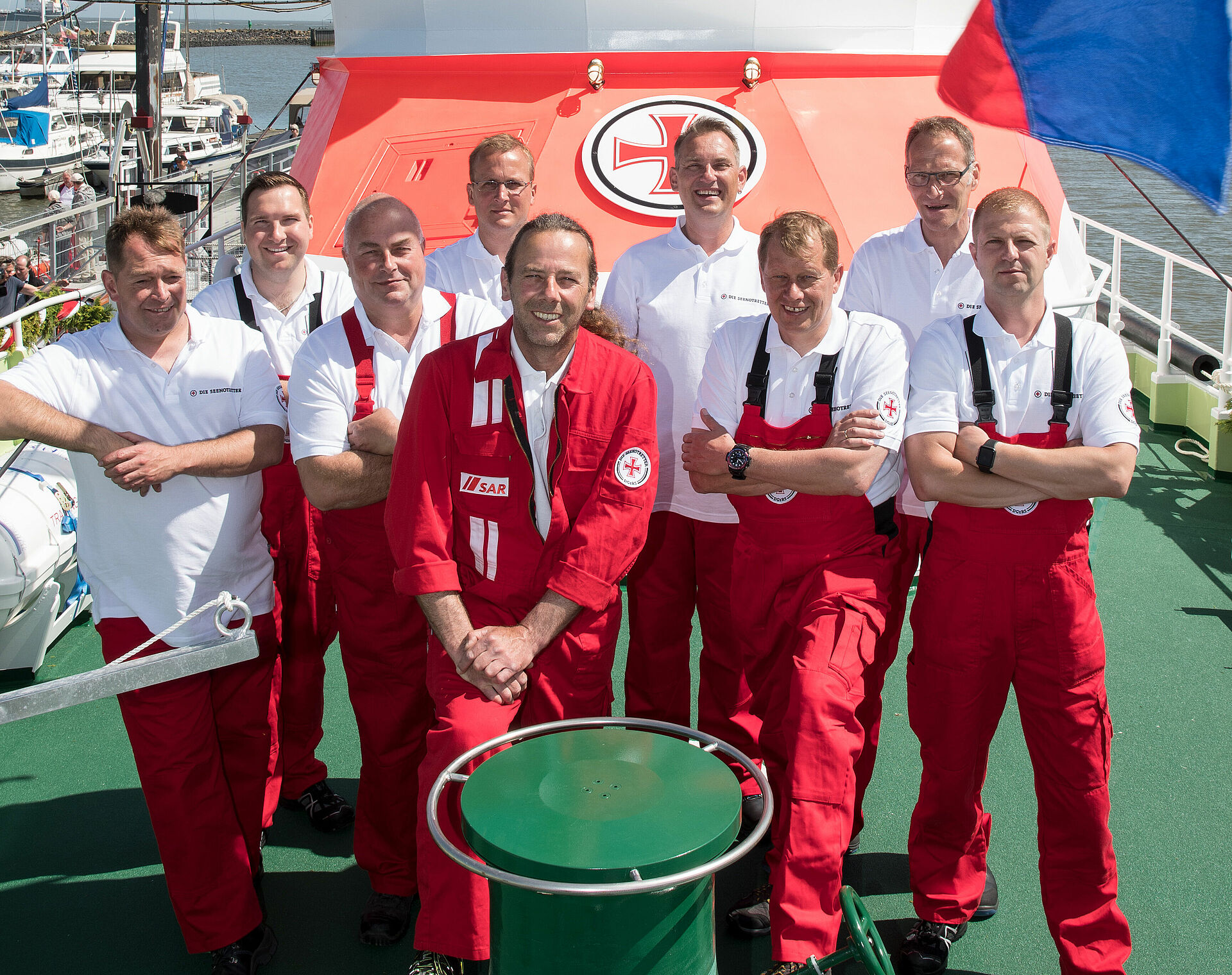 Gruppenbild der Seenotretter aus Cuxhaven auf dem Vorschiff ihres Seenotrettungskreuzers. Sie tragen rote Einsatzkleidung und lächeln freundlich in die Kamera.
