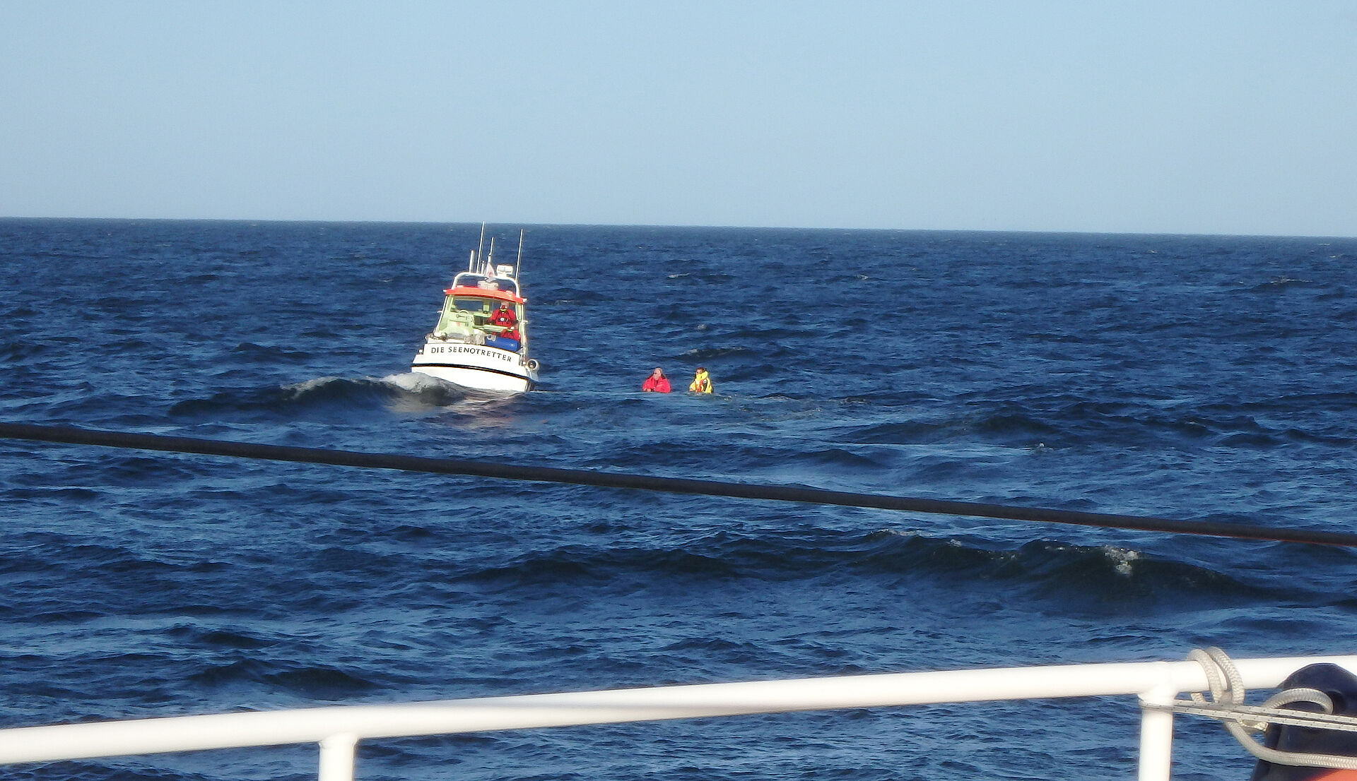 Zwei Menschen im Wasser neben dem Tochterboot eines Seenotrettungskreuzers.