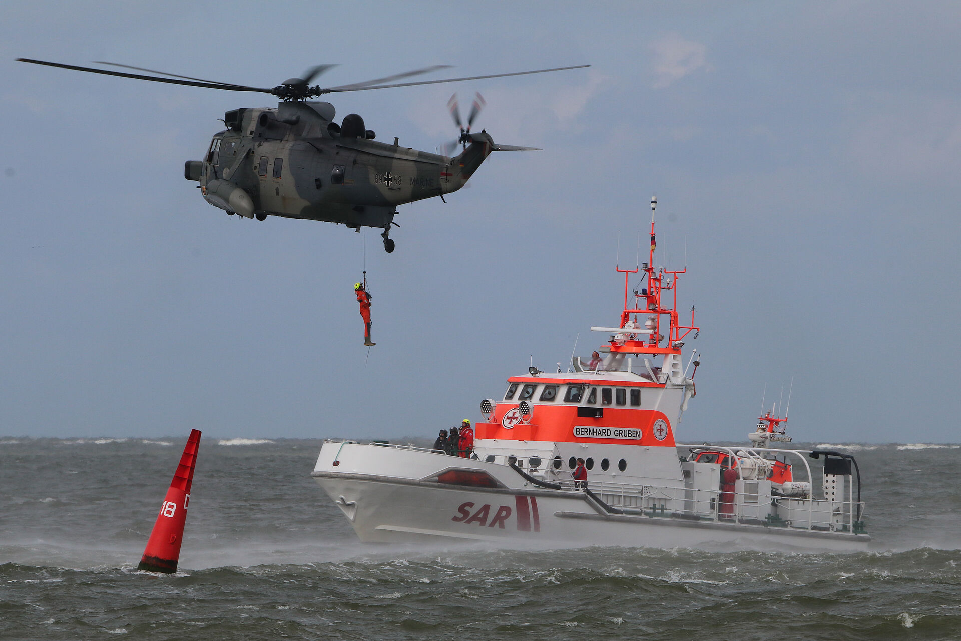 Seenotretter seilt sich von Hubschrauber ab, um auf Seenotrettungskreuzer zu landen
