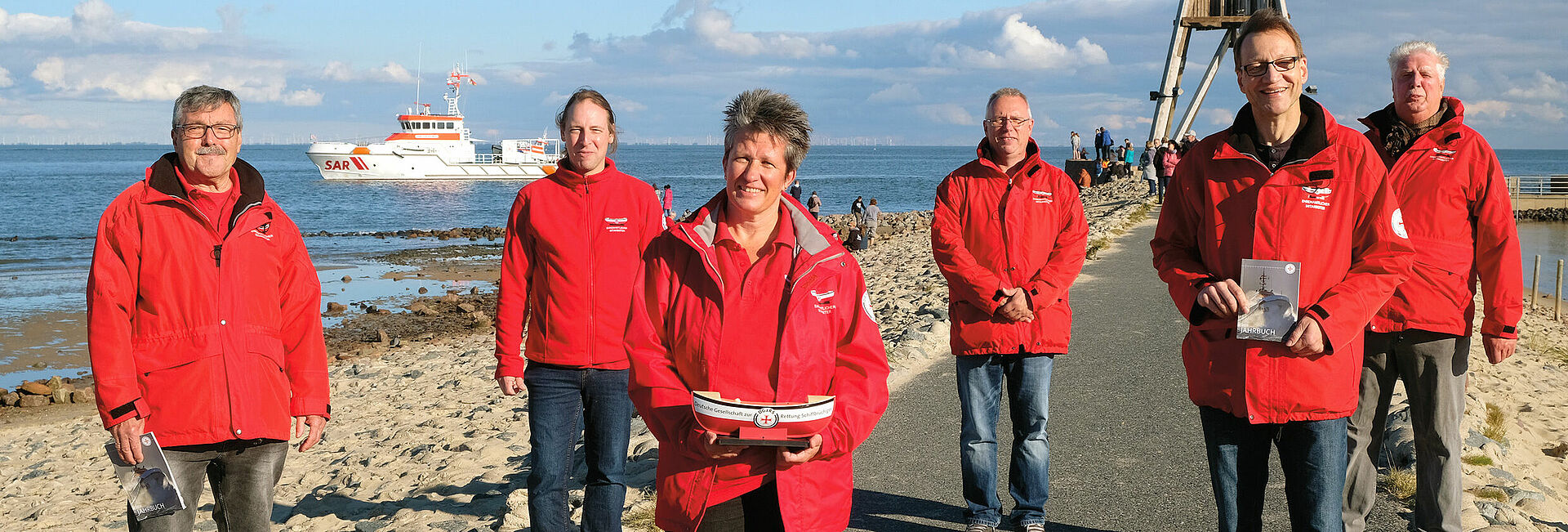 Sechs Ehrenamtliche stehen vor der Kugelbake in Cuxhaven