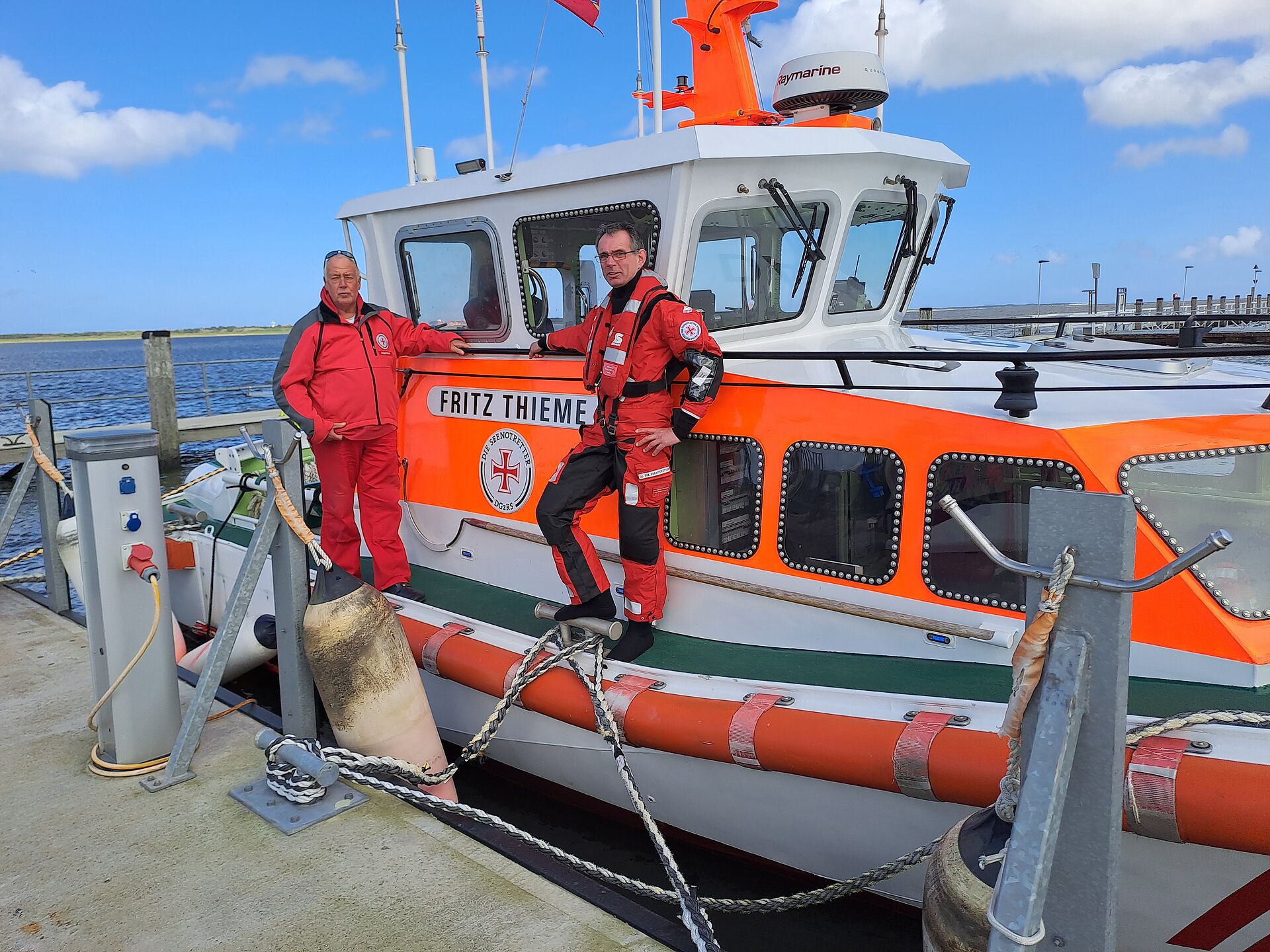 Vormann Bernd Abels (r.) und sein Vorgänger Roger Riehl in roter Dienstkleidung auf dem Seenotrettungsboot FRITZ THIEME.