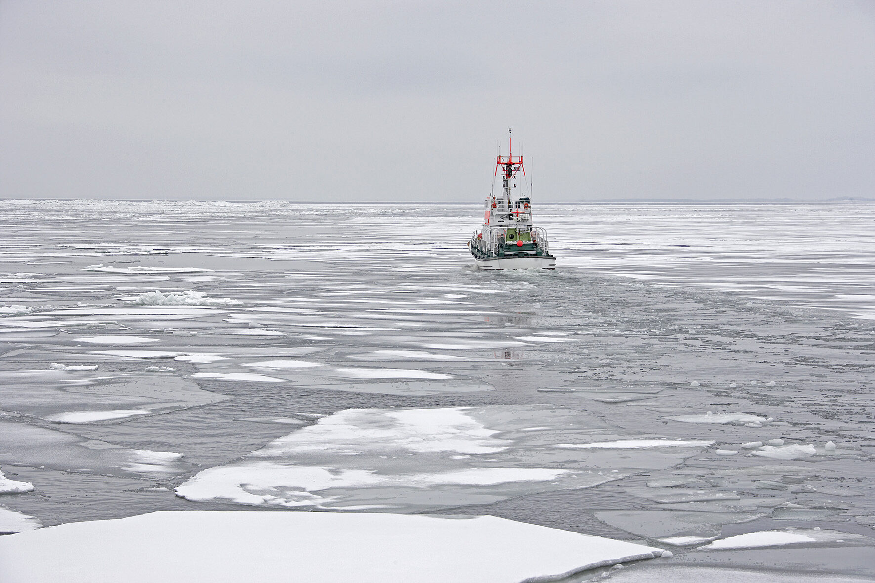 Heckansicht eines Seenotrettungskreuzers der bei trübem Wetter durch mit Schnee bedeckten Eisschollen fährt.
