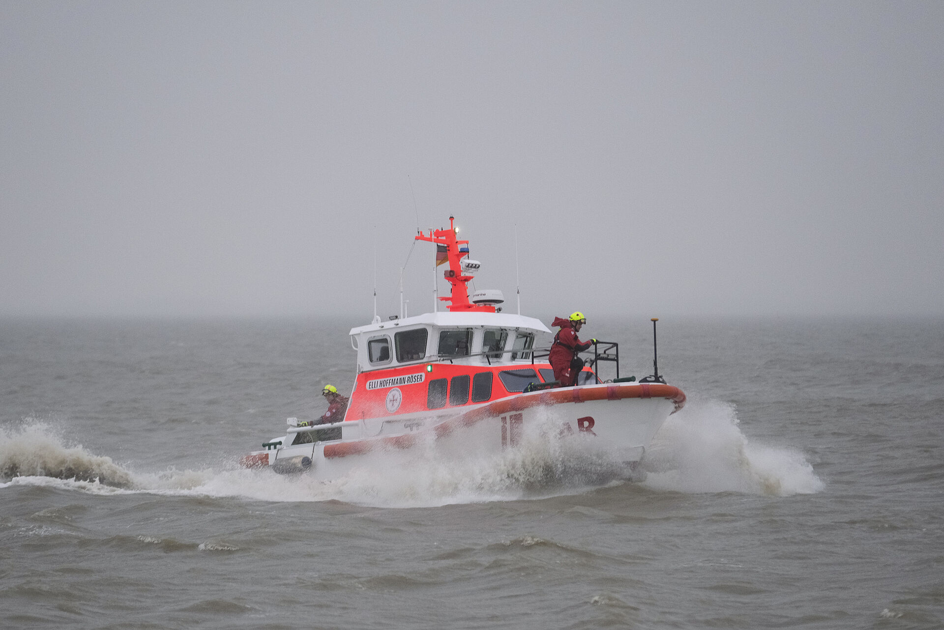 Ein Seenotrettungsboot fährt bei nebeligem Wetter durch die Nordsee. Auf dem Vorschiff kniet ein Seenotretter in rotem Überlebensanzug.