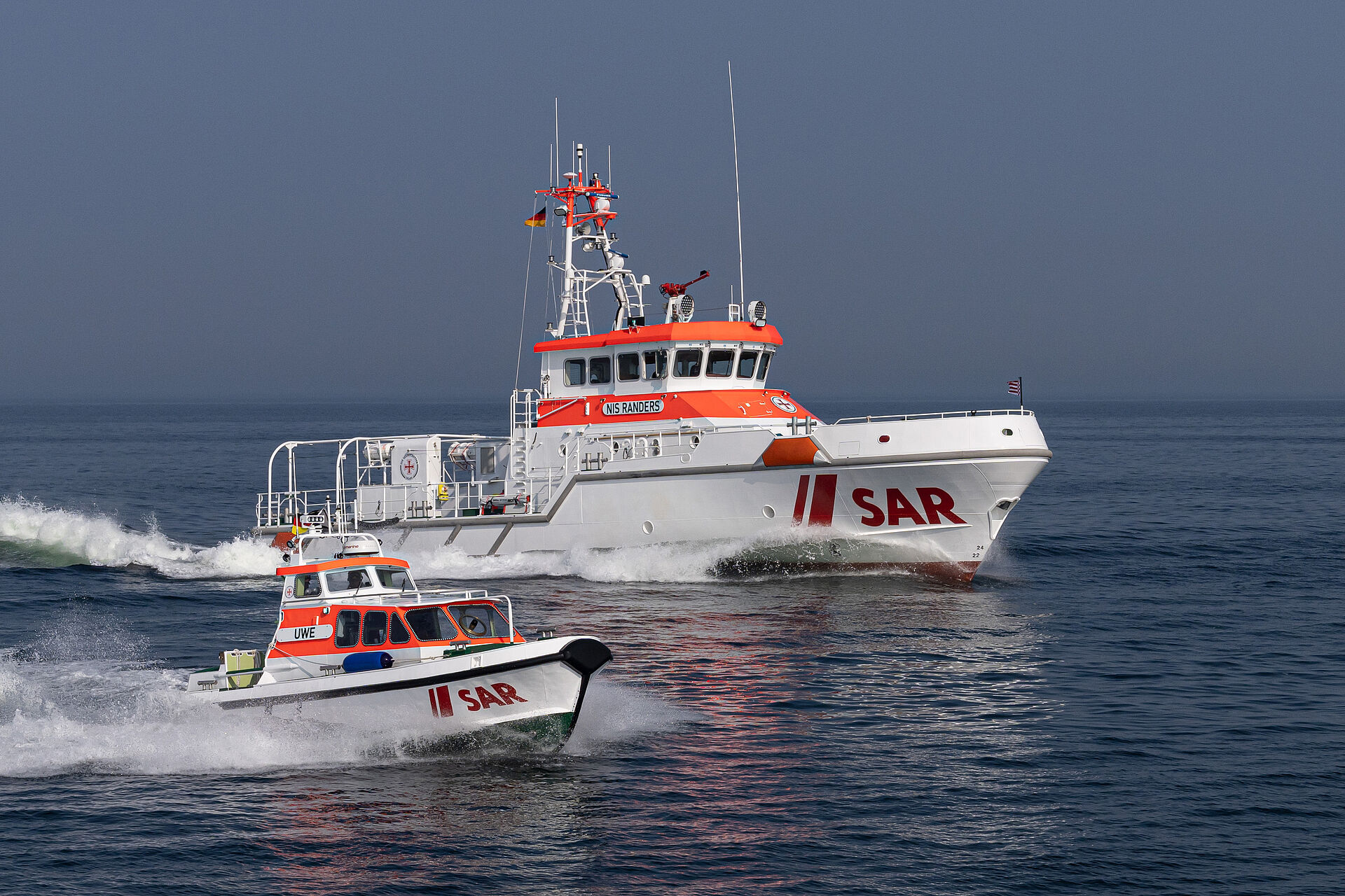 Ein Seenotrettungskreuzer und sein Tochterboot fahren parallel mit hoher Geschwindigkeit über das Meer.