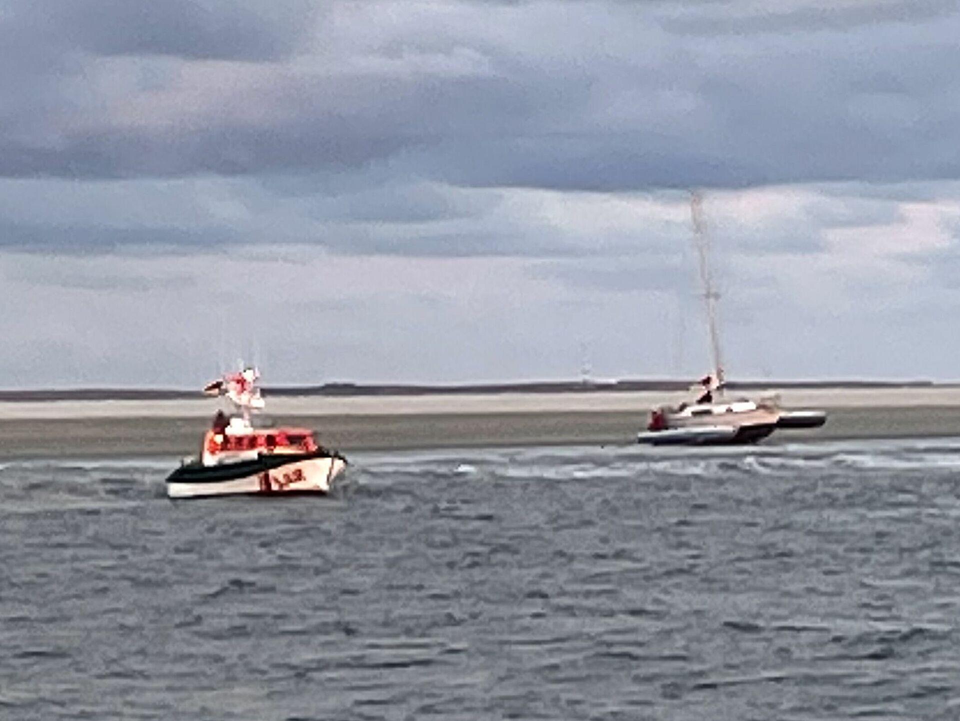 Das Tochterboot eines Seenotrettungskreuzers nahe einem gestrandeten Trimaran auf der Nordsee