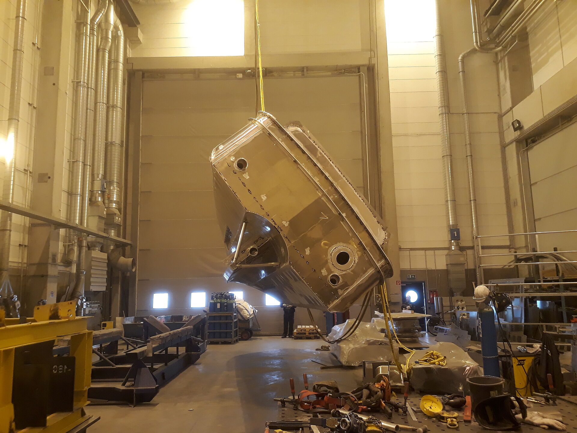 Der Rohbau aus Aluminium eines Seenotrettungsbootes wird in einer Werfthalle von einem Hallenkran um die Längsachse gedreht. Ansicht von hinten.
